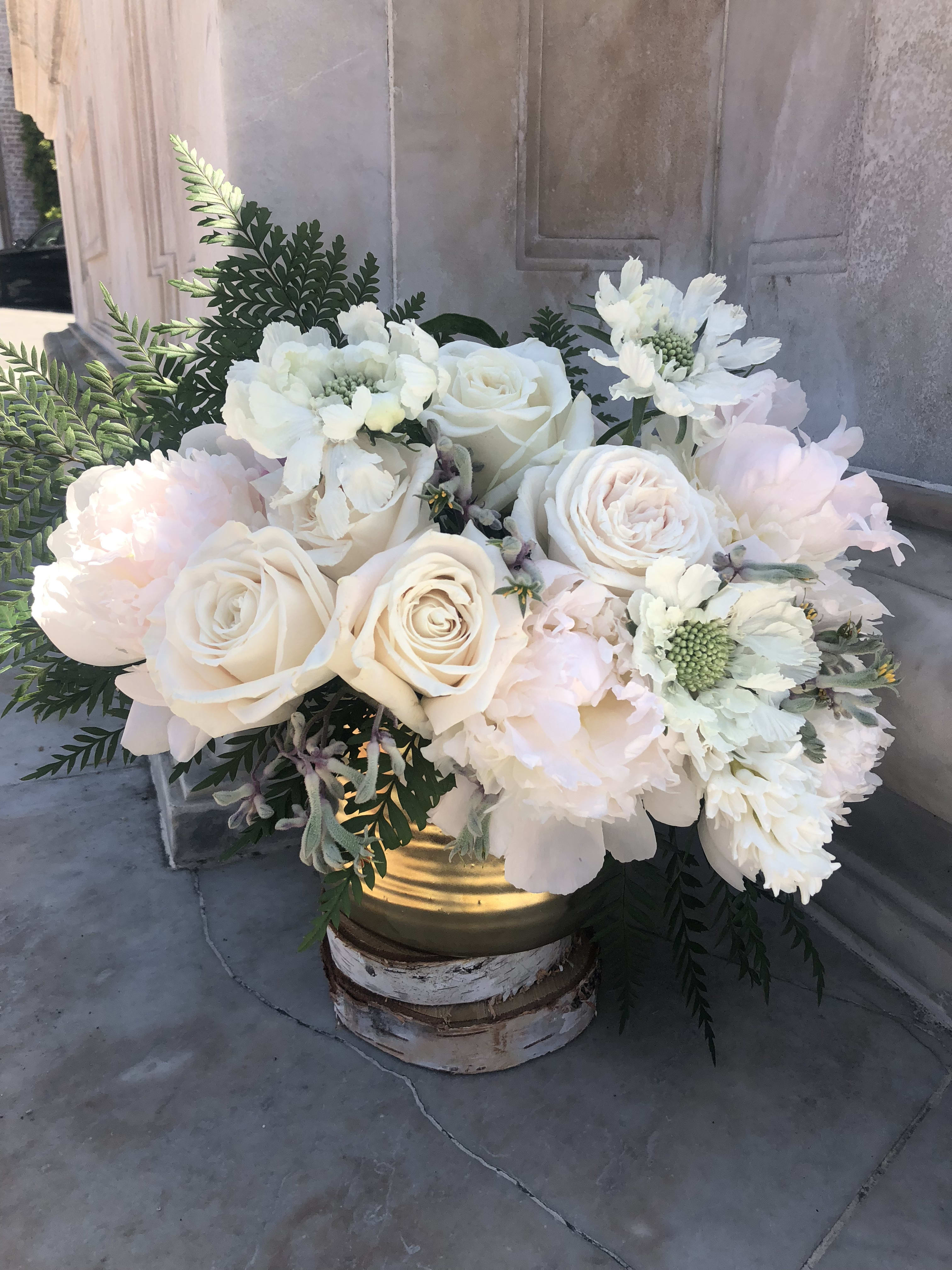 Ivory and white rose and peony arrangement with ferns in a gold container on a wood base