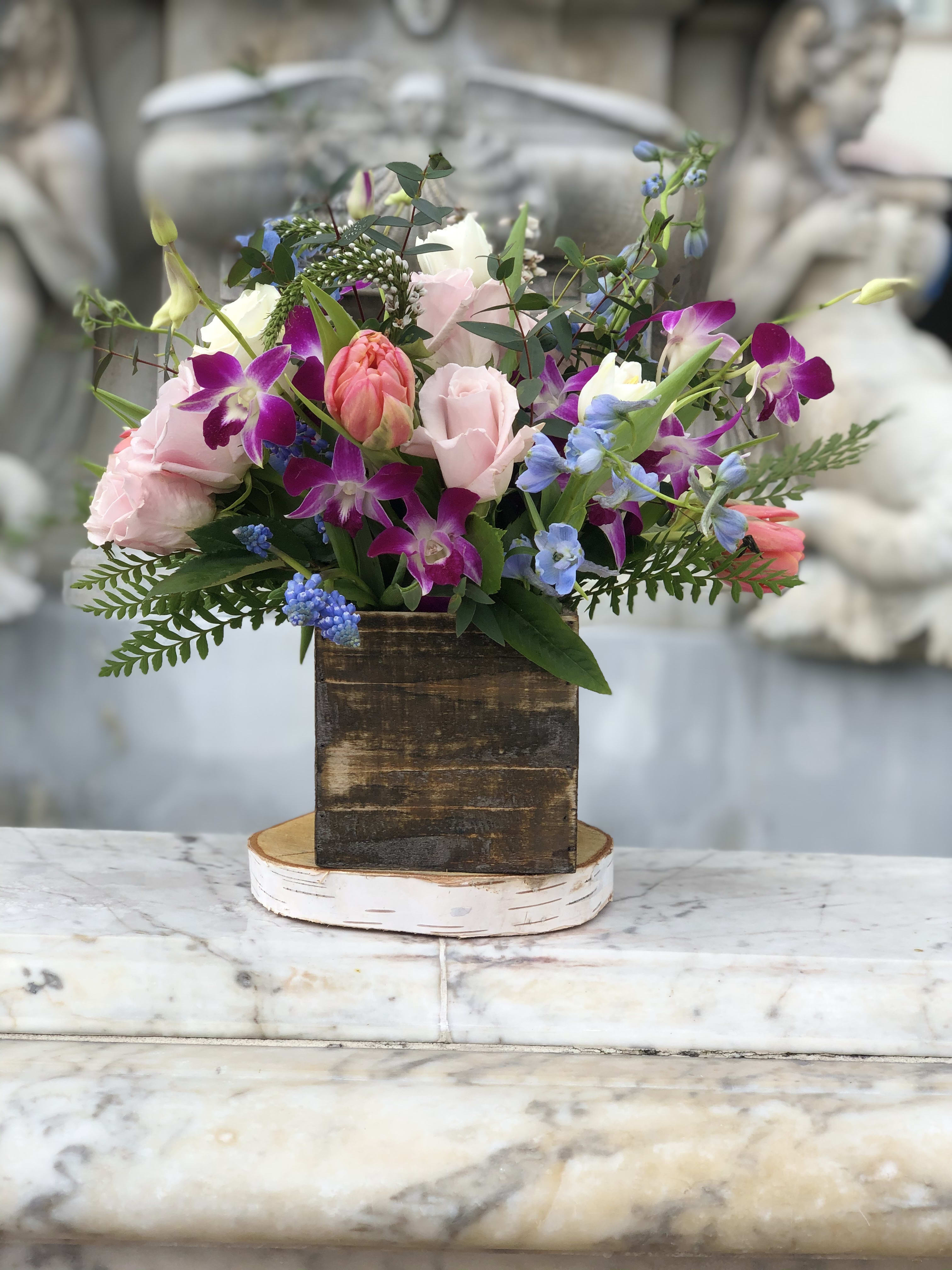 Rustic wood box arrangement with pink roses, tulips, purple orchids, and blue blooms