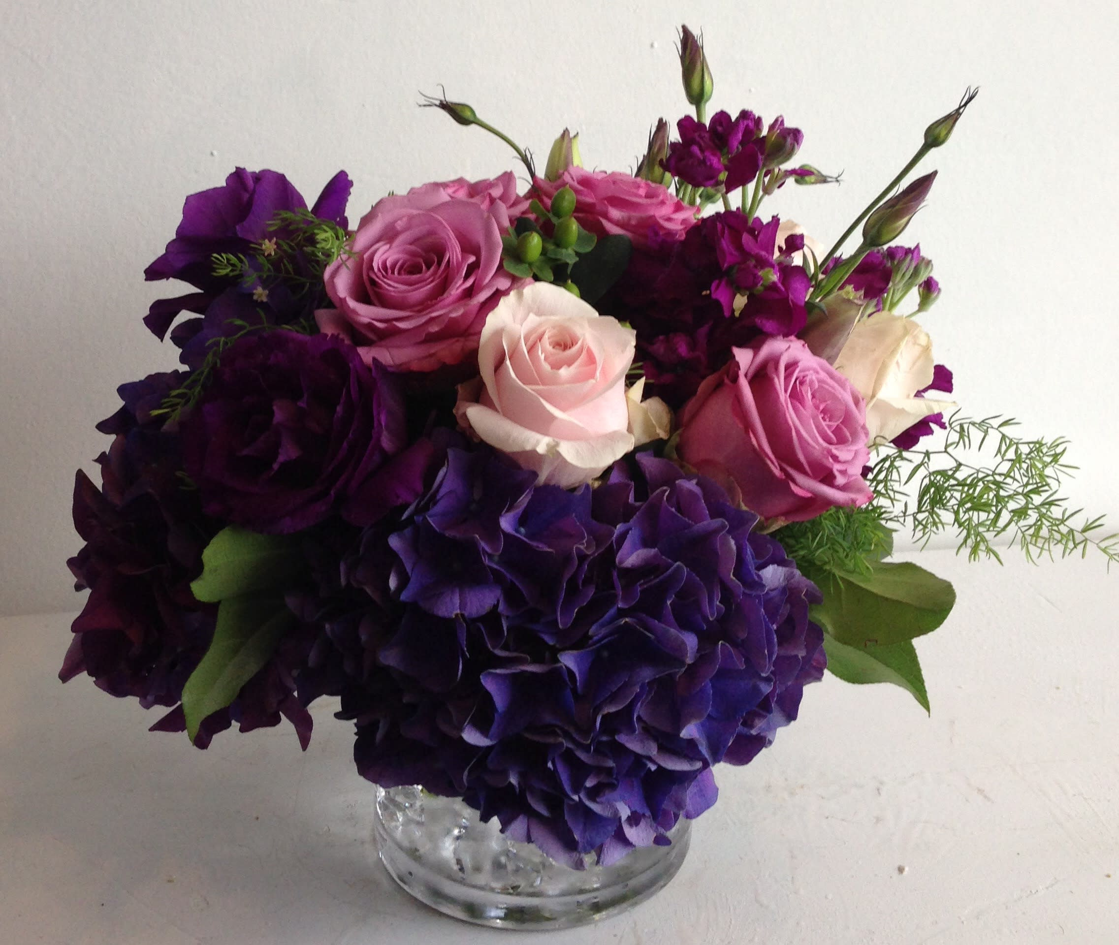 Purple and pink roses with hydrangeas in a clear glass vase