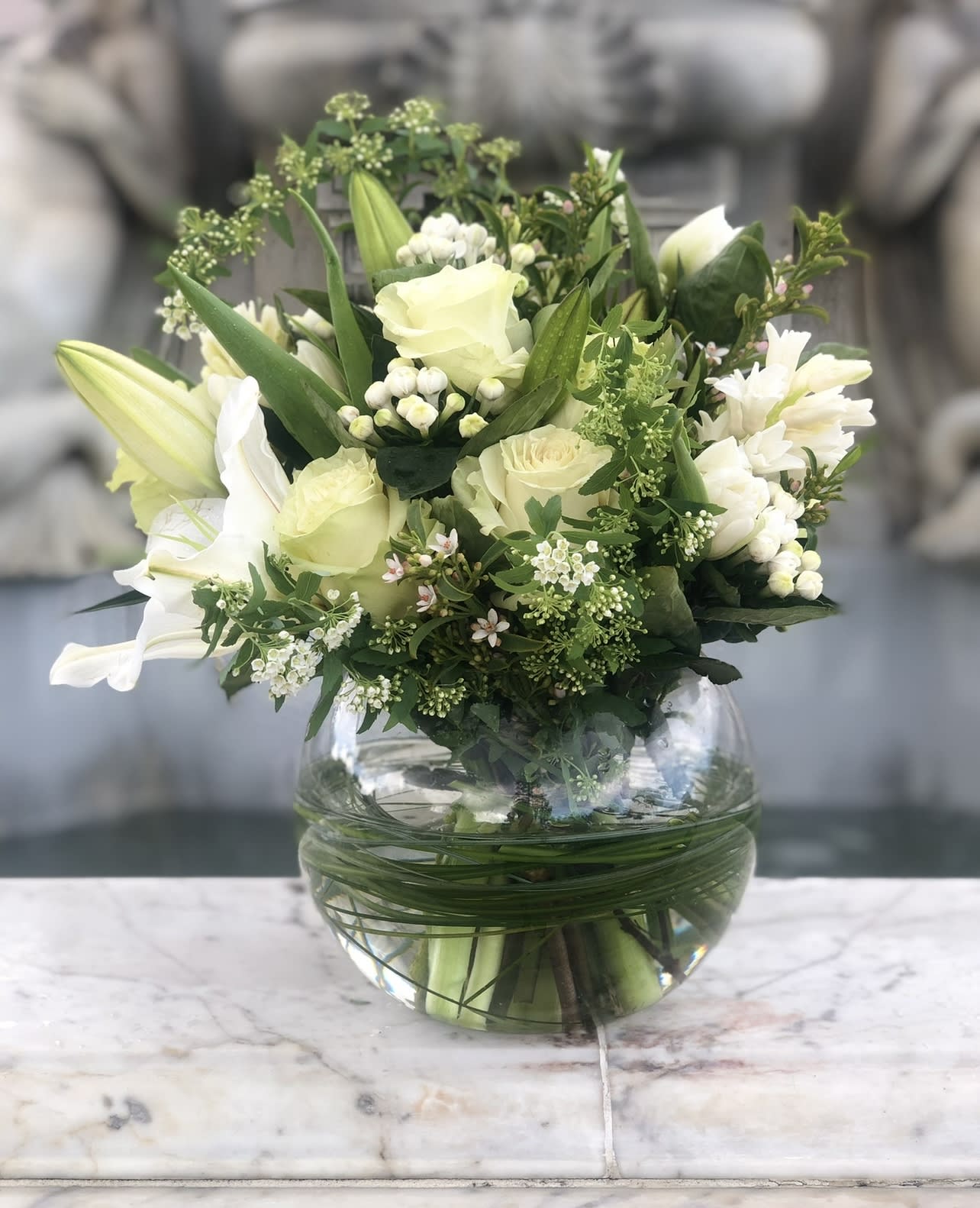 White and pale green floral arrangement in a round glass vase