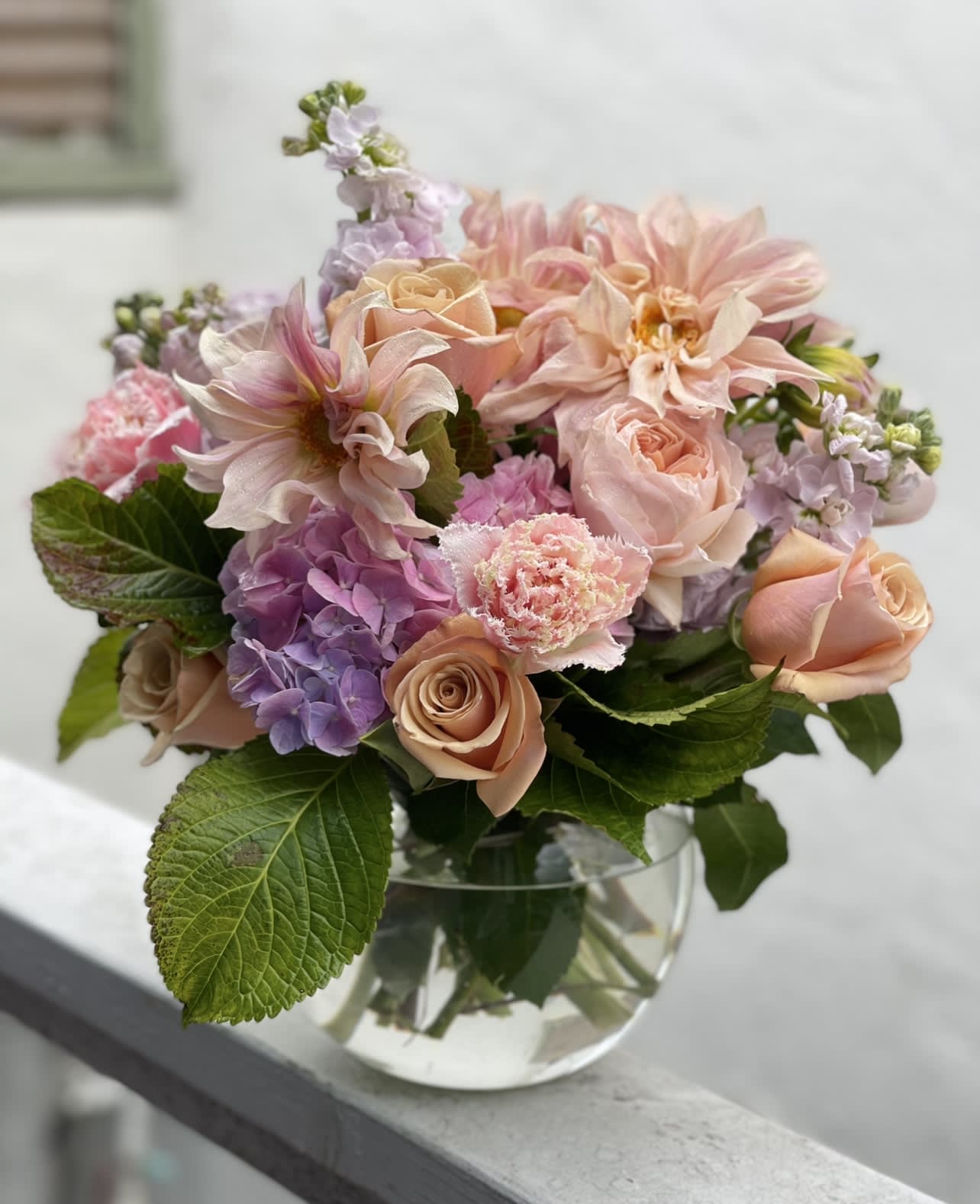Low glass vase of peach roses, pink dahlias, and purple hydrangea with lush foliage