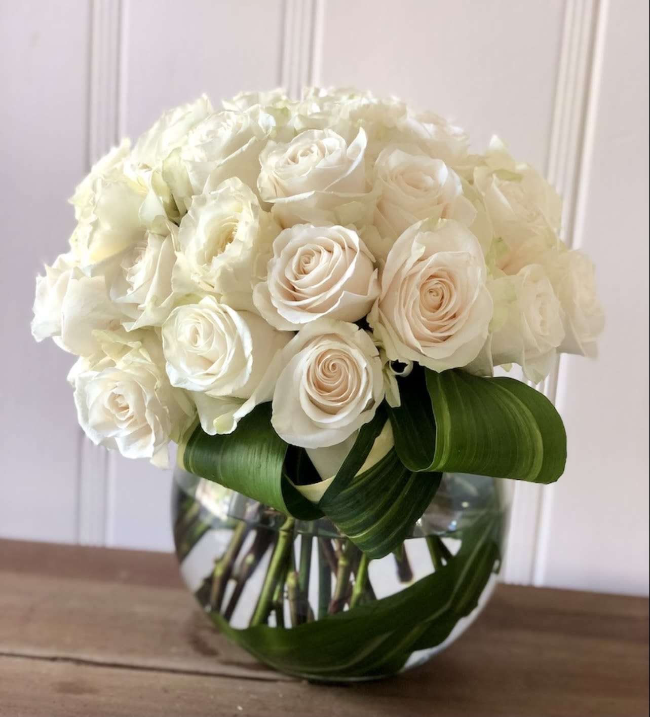 White rose bouquet in a clear glass vase with broad green leaves