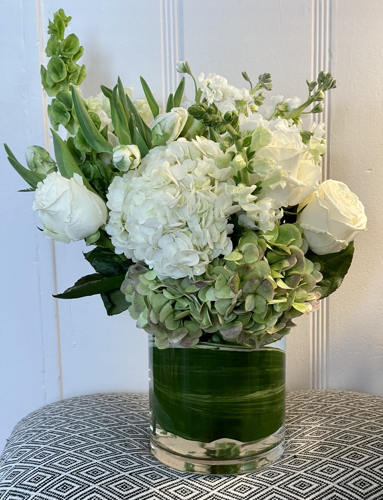 MAGIC OF WHITES - White flowers are beautiful. This design with both white and soft green hydrangeas, and bells of Ireland with the most beautiful playa Blanca roses is stunning. It comes in a 6x5 clear glass container lined with beautiful tea leaves.