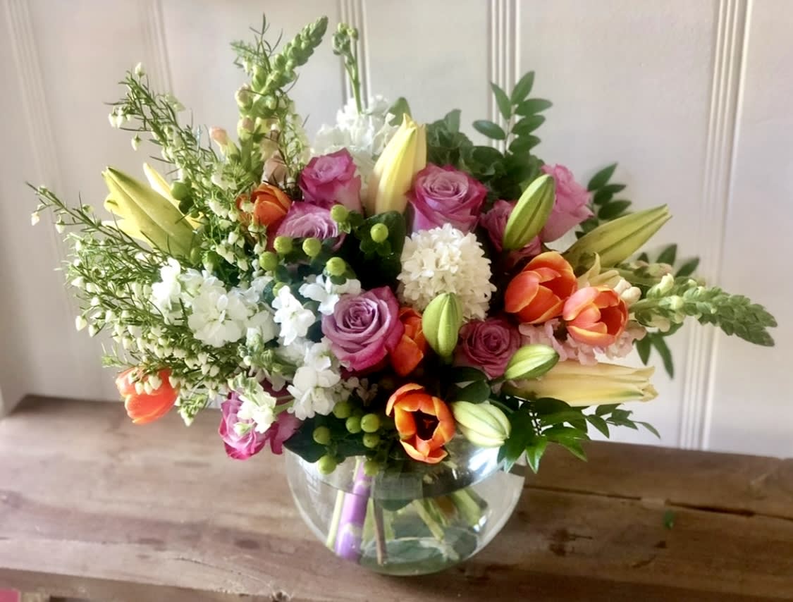 Mixed bouquet of roses, lilies, and tulips in a glass bowl vase