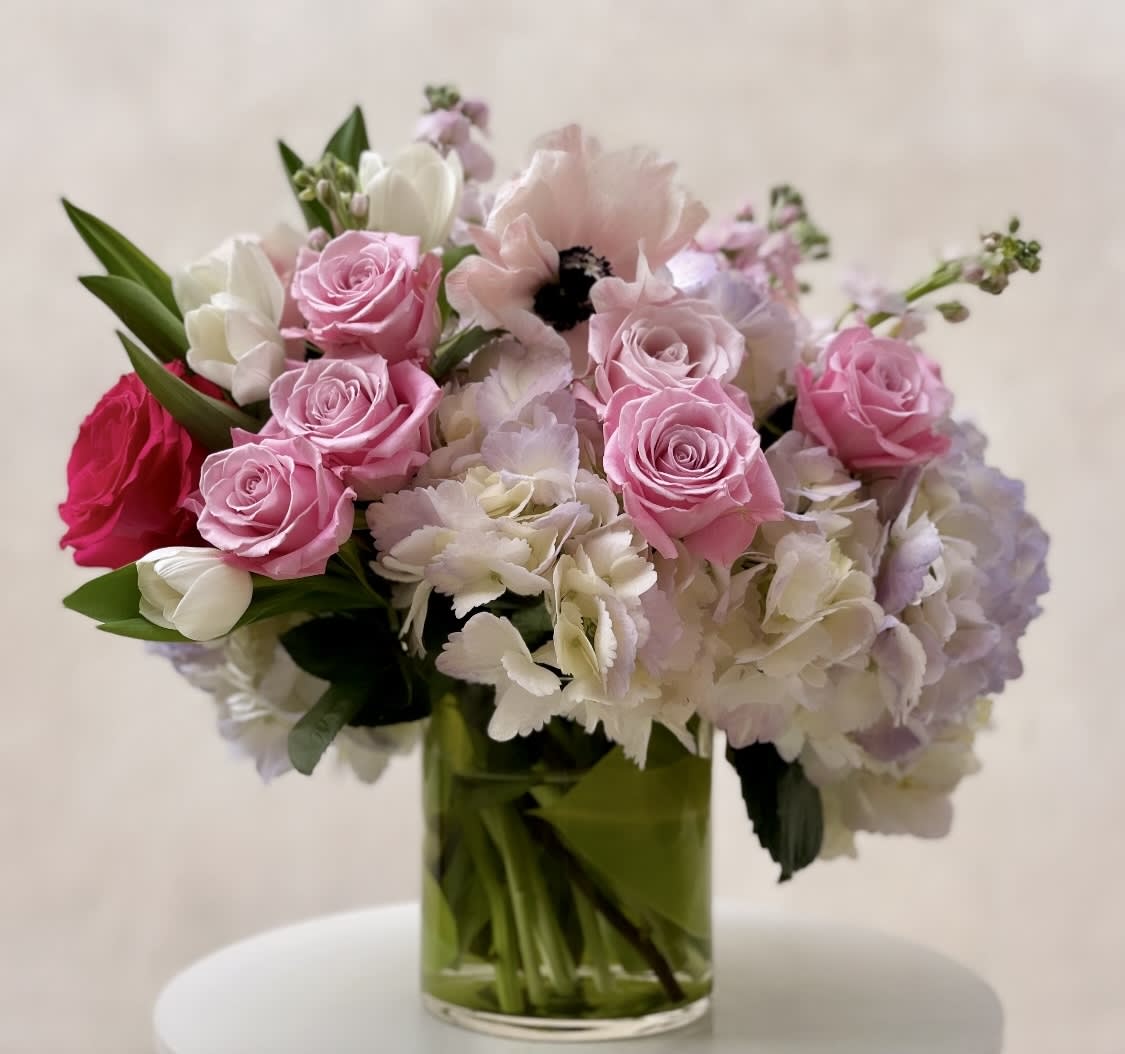 Pink roses, white tulips, anemones, and pastel hydrangeas in a clear glass vase