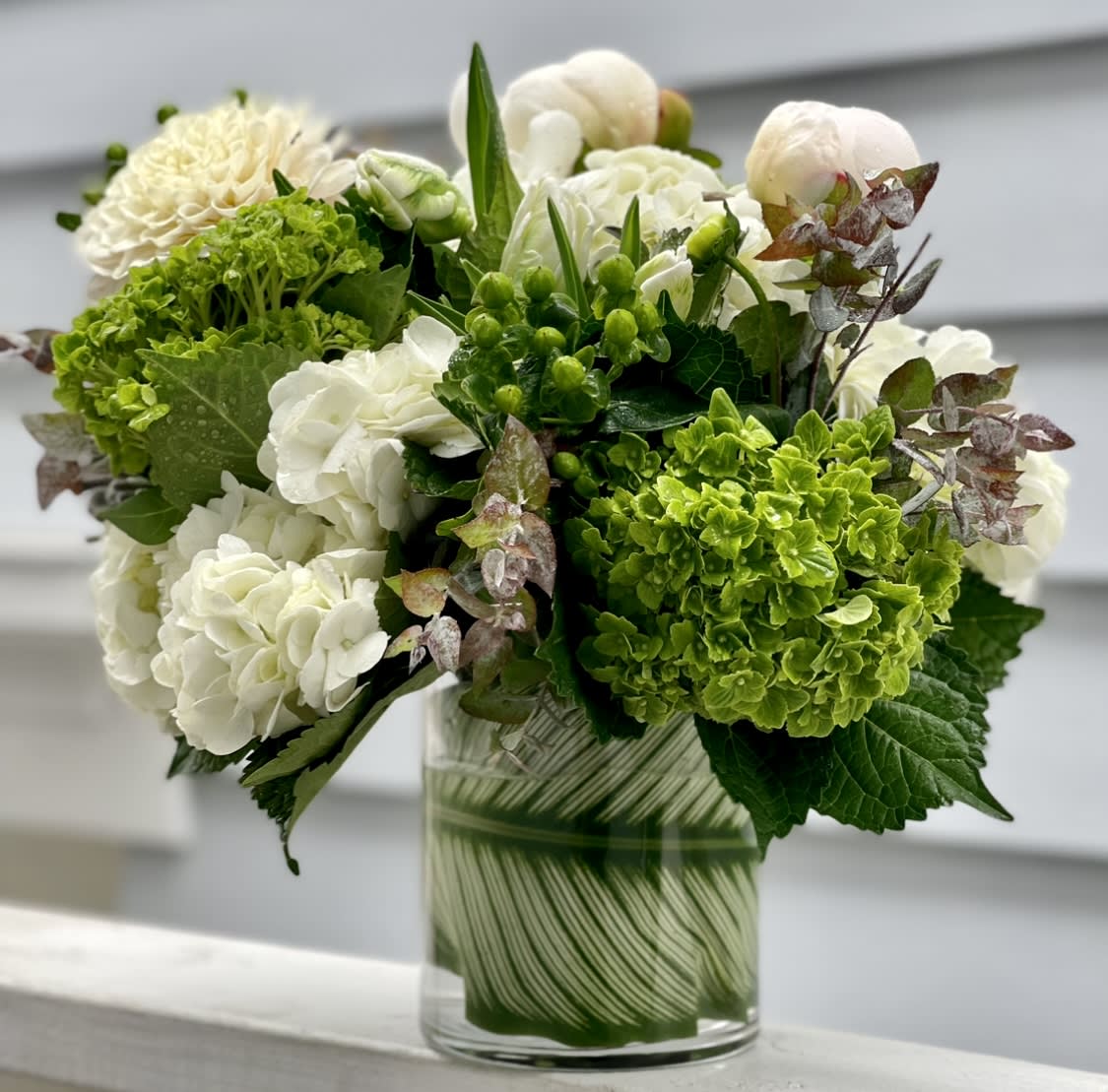 Compact arrangement of white and green blooms in a clear glass cylinder vase