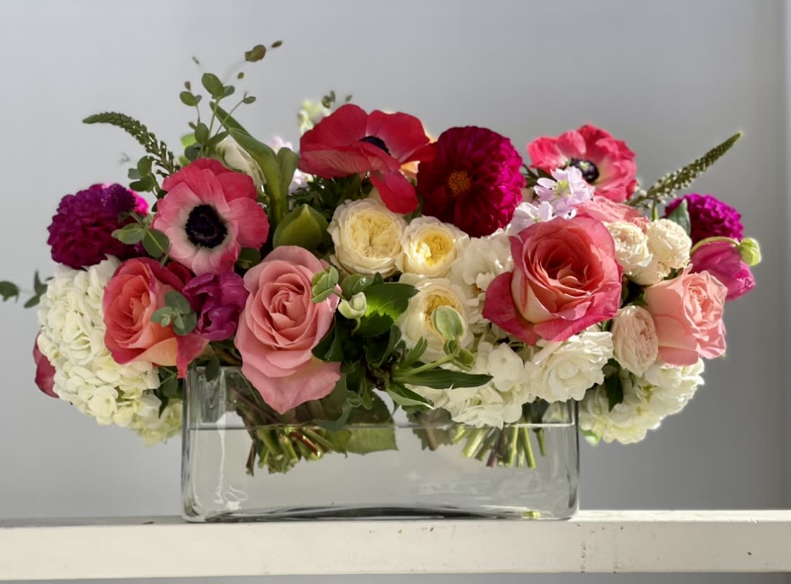 Low rectangular arrangement of pink, red, and white flowers in a clear glass vase