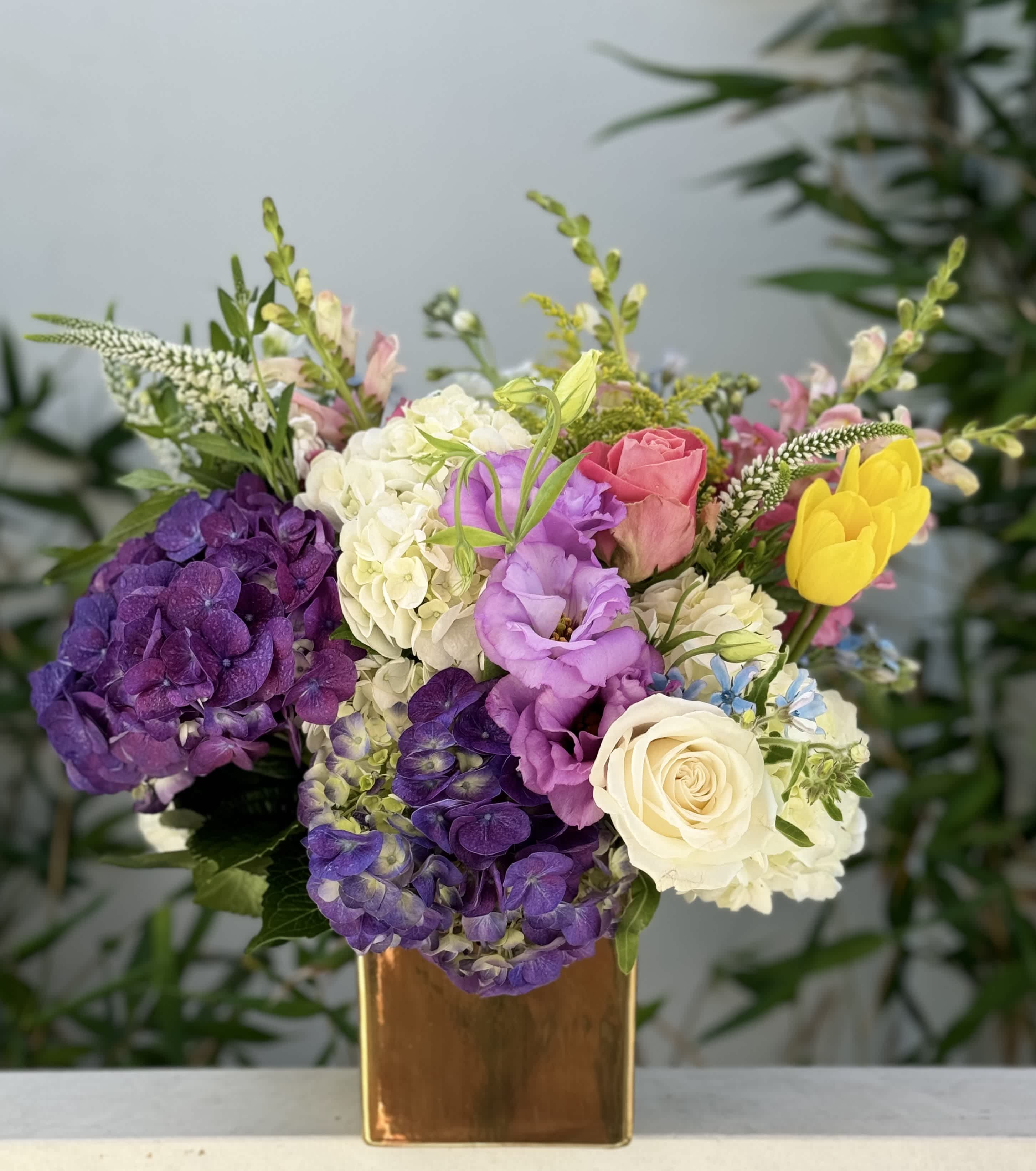 Colorful bouquet in a gold vase with purple hydrangeas, roses, and yellow tulips