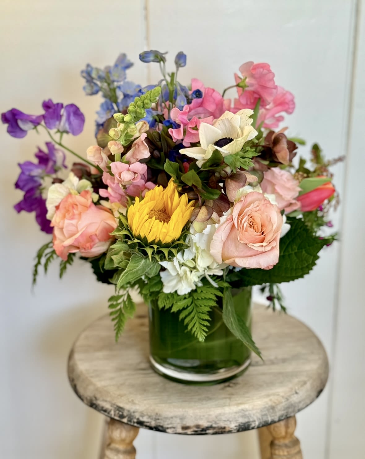 Mixed bouquet in a green glass vase with pink, purple, blue, and yellow flowers