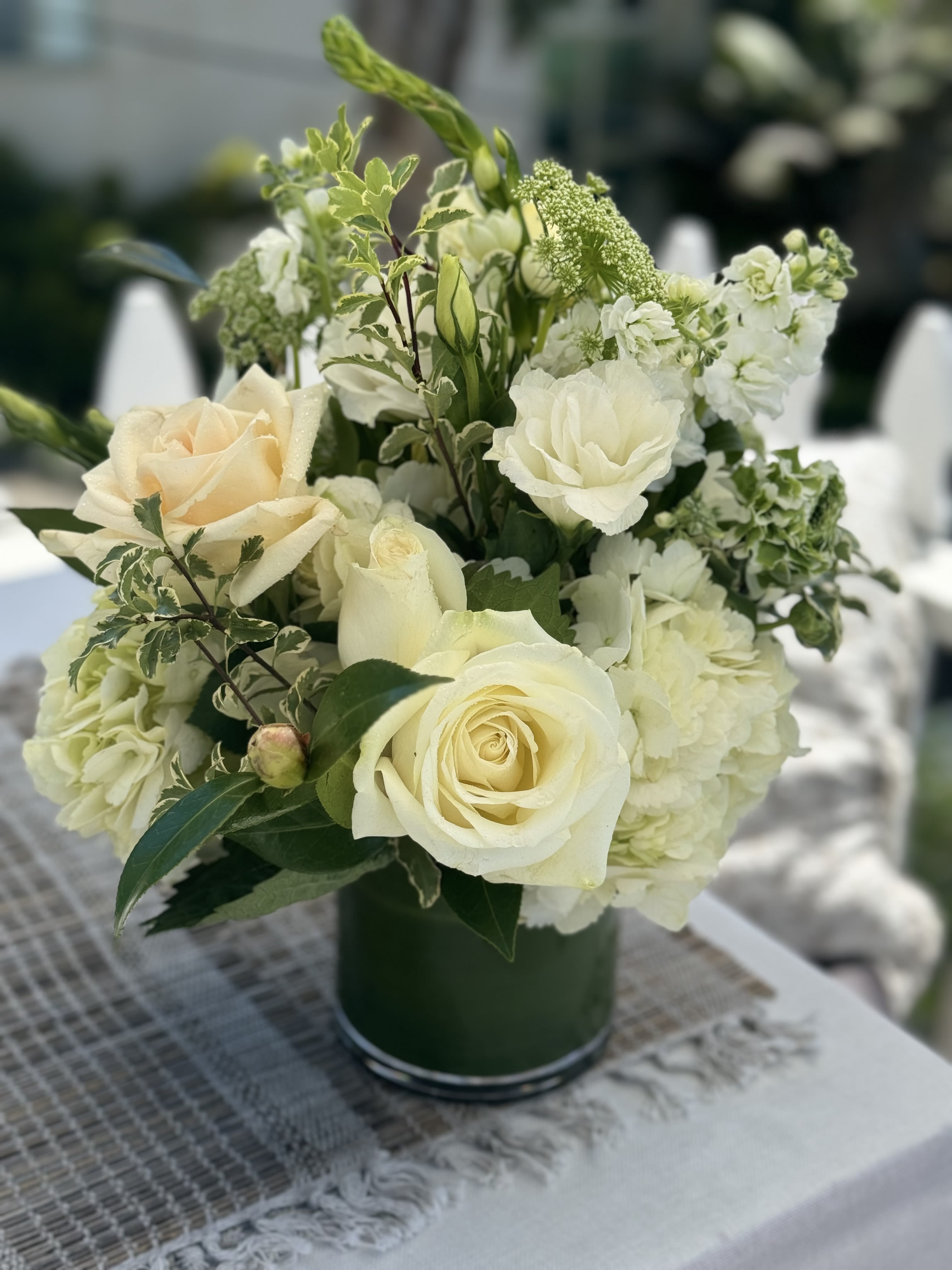 PURE AND SIMPLE  - This beautiful whites and green design is anything but simple. It’s elegant yet casual enough to accent any beach or even non beach home. Bringing beautiful roses, ranunculous, lisianthus and verigated greens. You simply can’t go wrong with this one!