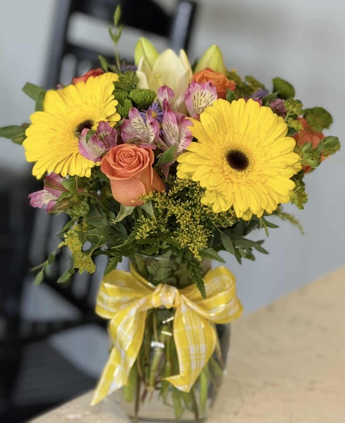 Bouquet of yellow gerbera daisies and peach roses in a glass vase with a yellow ribbon