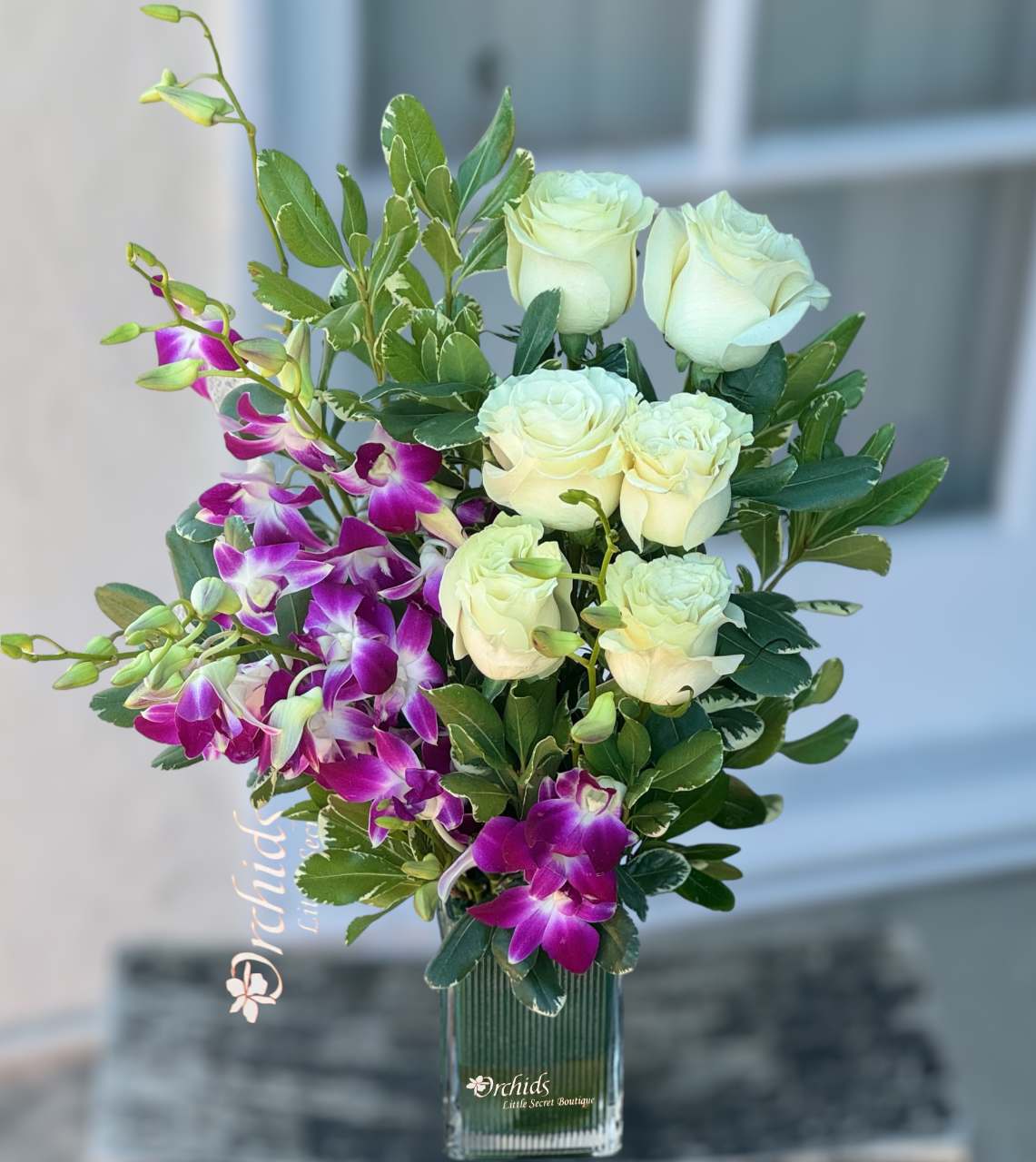 White roses and purple orchids arranged in a clear glass vase