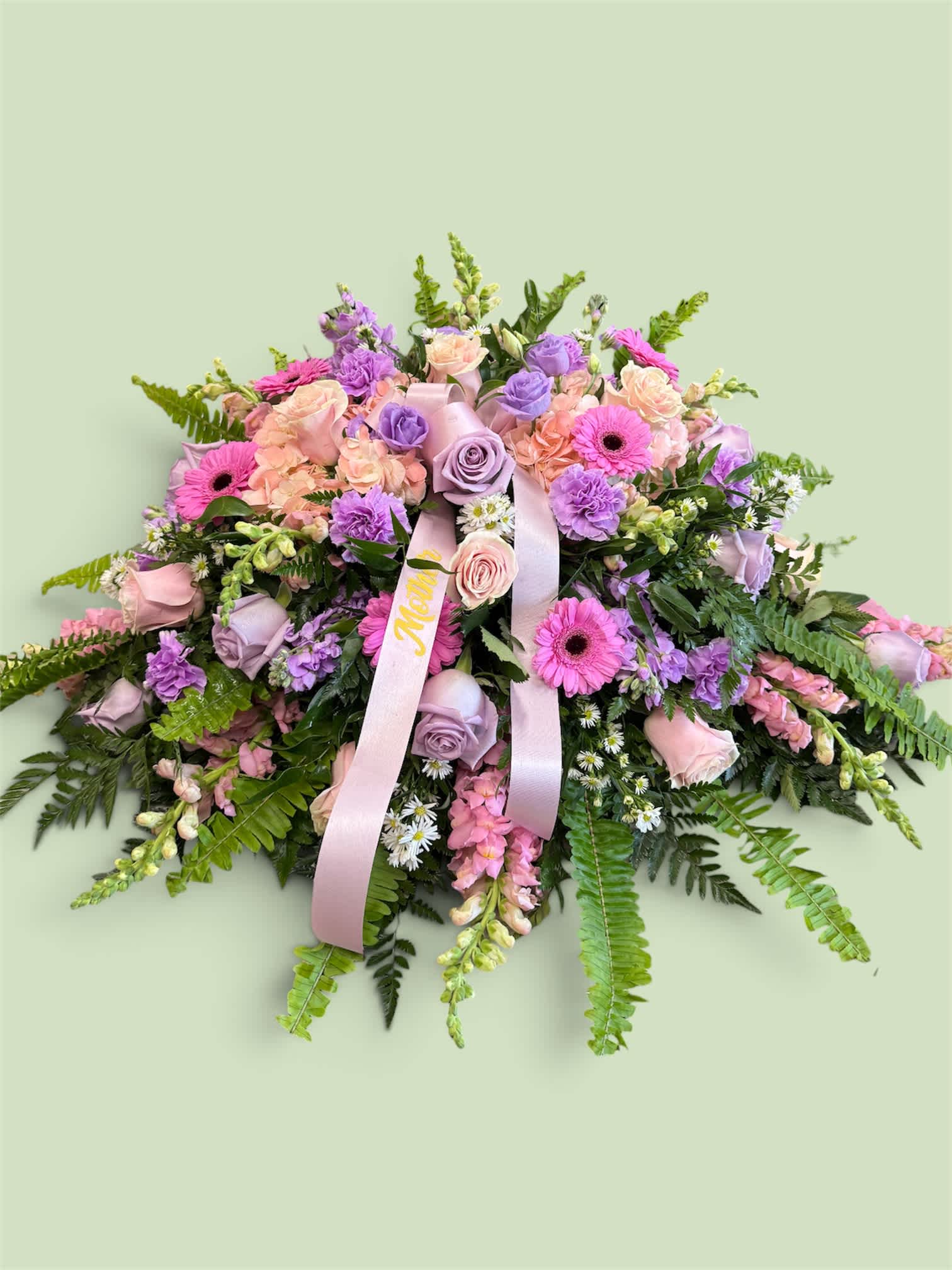 Pink and lavender floral arrangement with ribbon on a pale green background