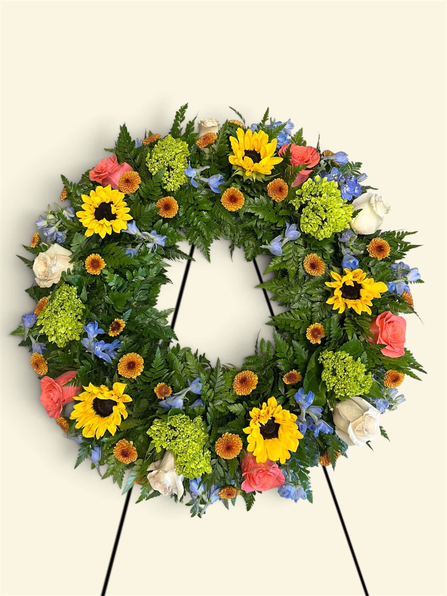 Circular floral wreath with sunflowers, roses, and blue flowers on a stand