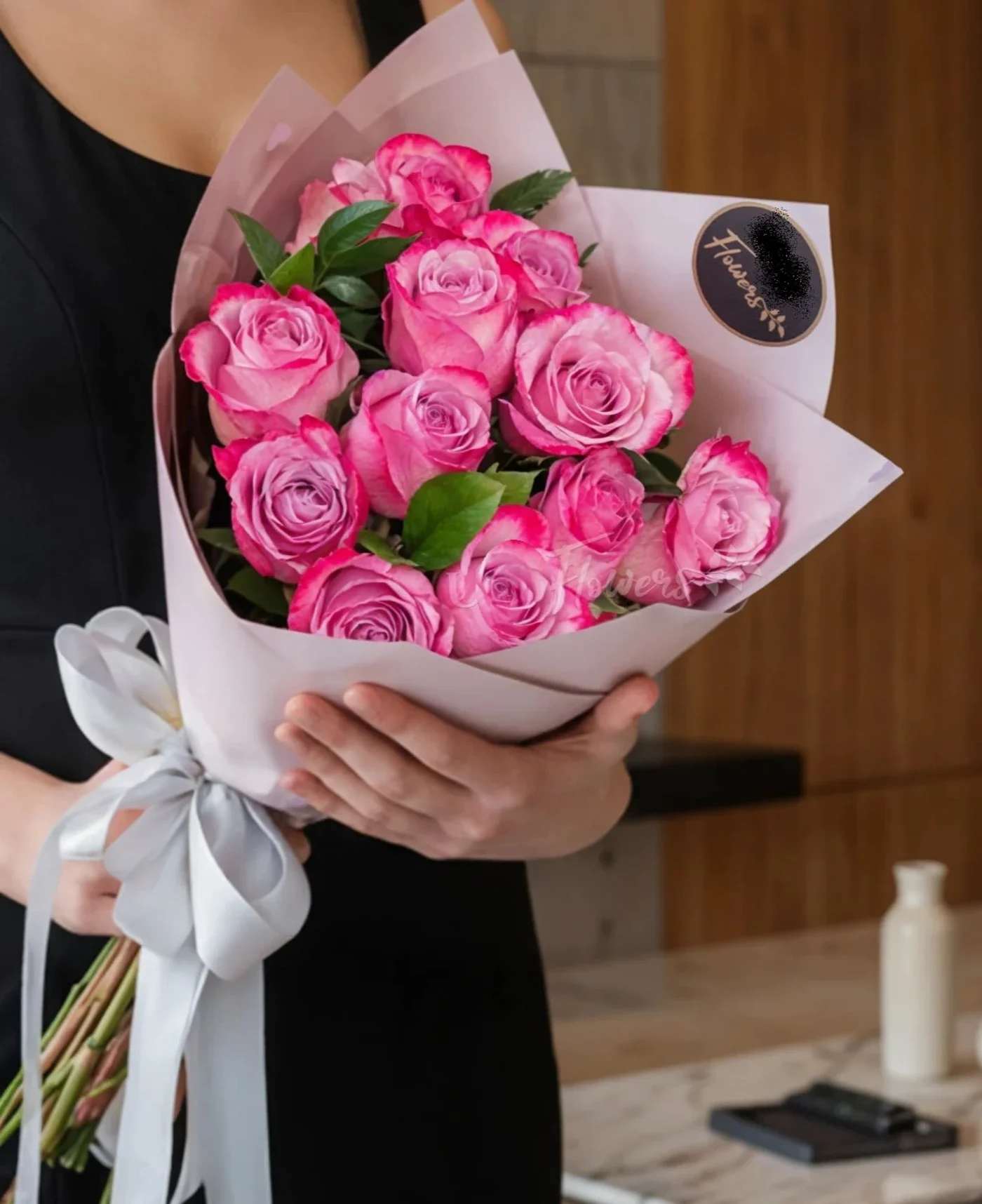 Bouquet of pink roses wrapped in pale paper with a white ribbon