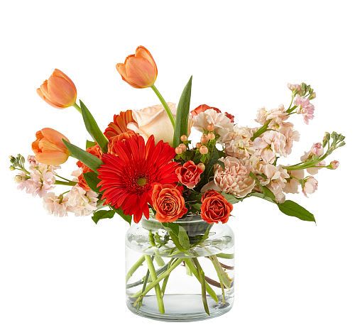 Mixed bouquet of orange tulips, red gerbera daisies, and peach roses in a glass vase