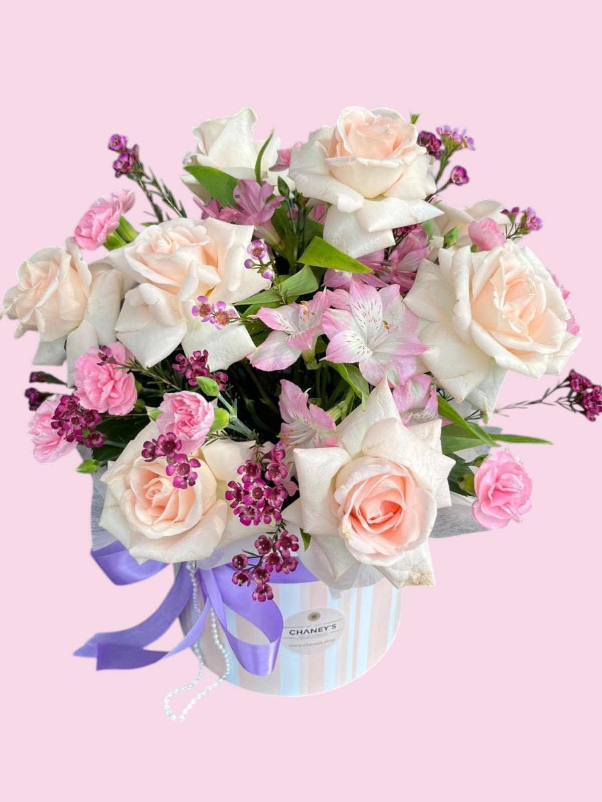 Pink and white roses arranged in a striped hat box with a purple ribbon
