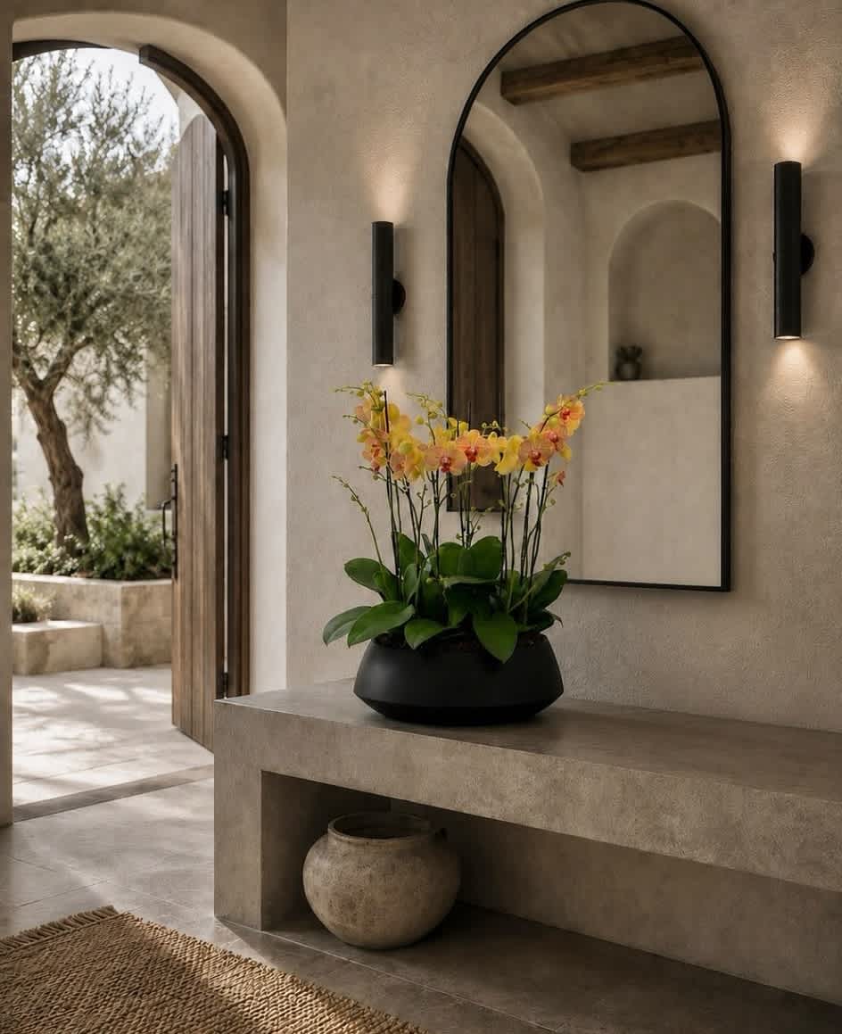 Orange and yellow orchids in a black bowl on a stone console