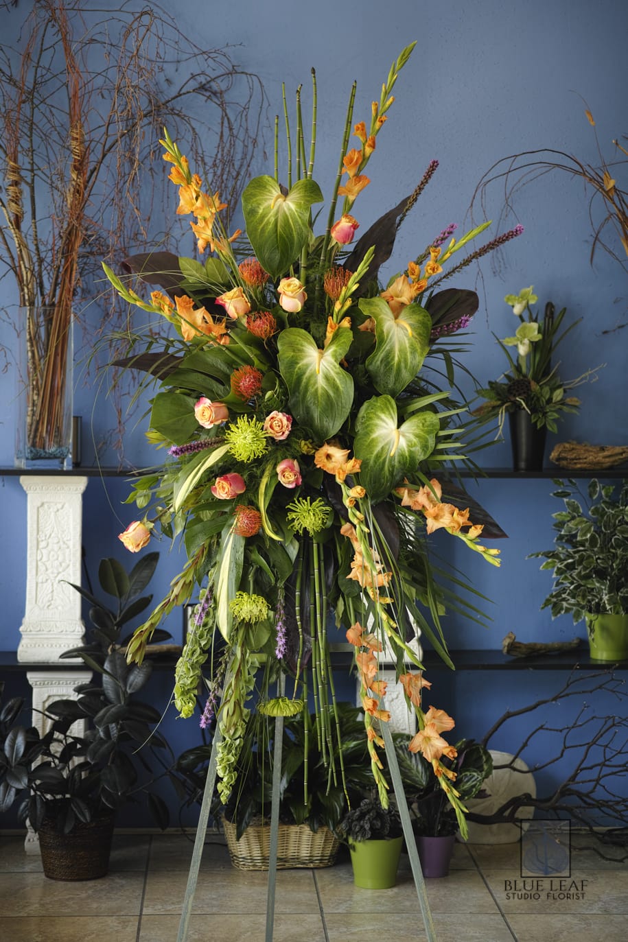 Tall tropical floral arrangement with orange blooms and large green leaves in a basket