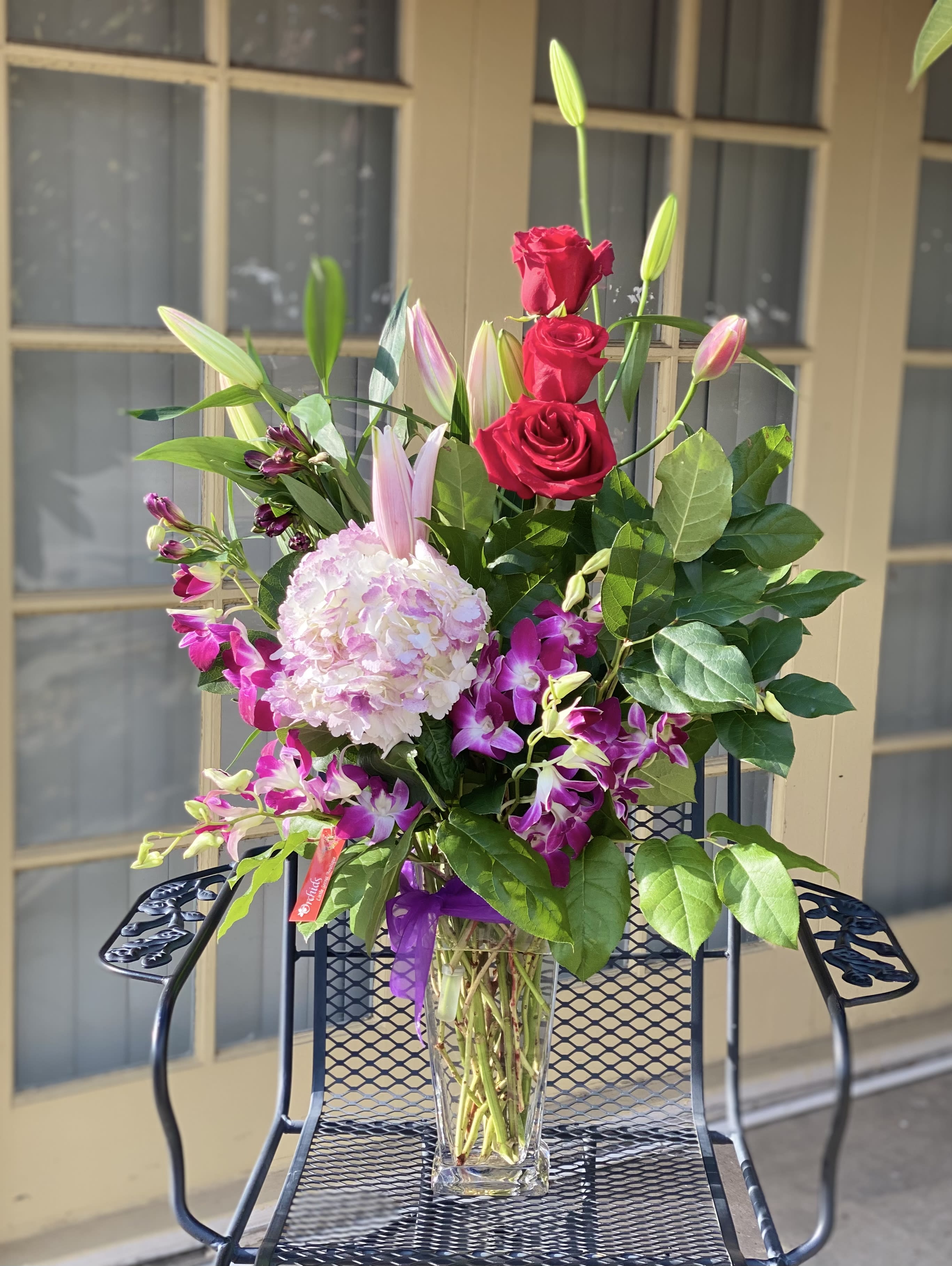 Bouquet of red roses, pink lilies, and orchids in a clear glass vase