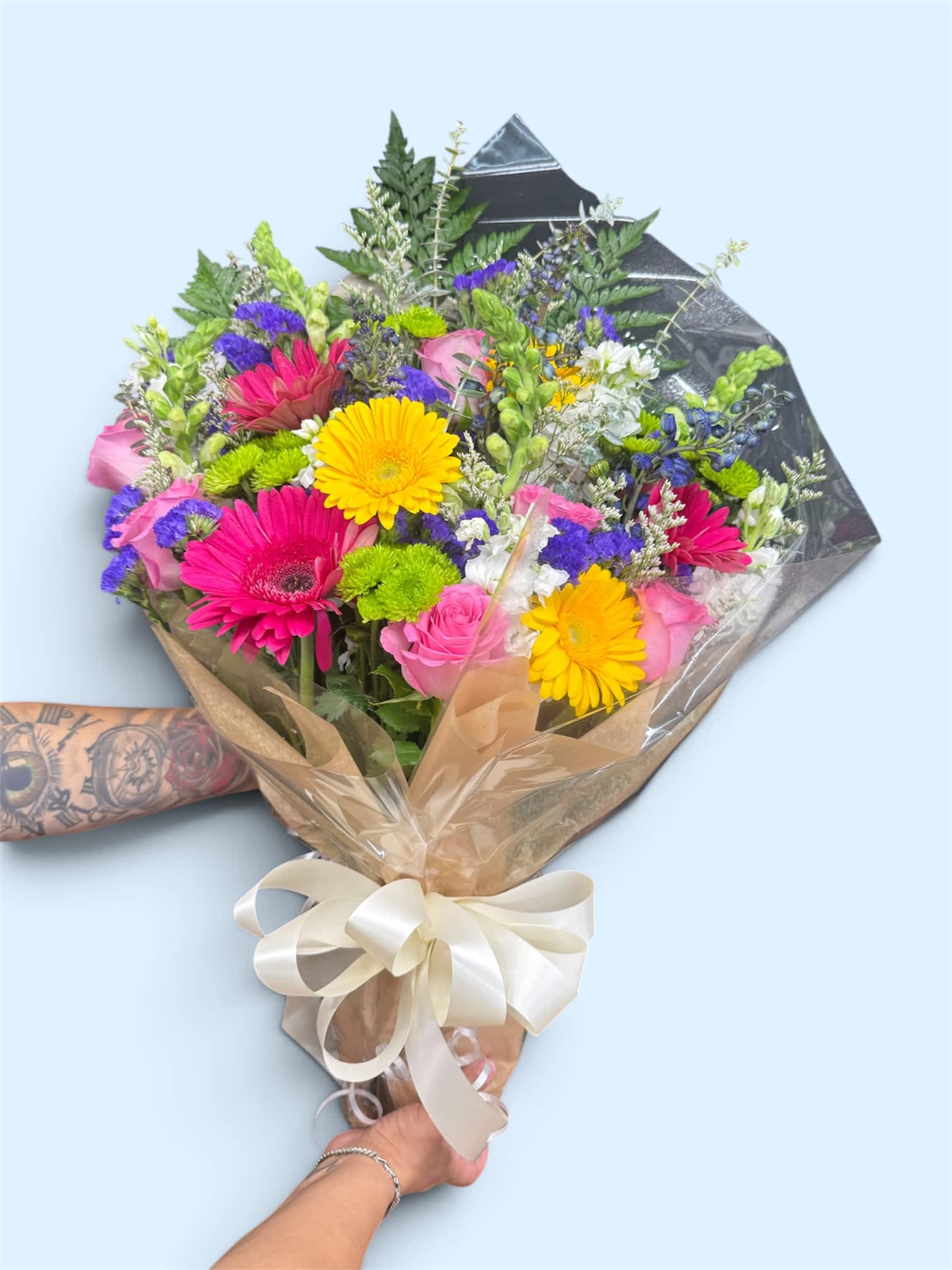 Mixed bouquet of pink, yellow, and purple flowers wrapped in paper with a ribbon