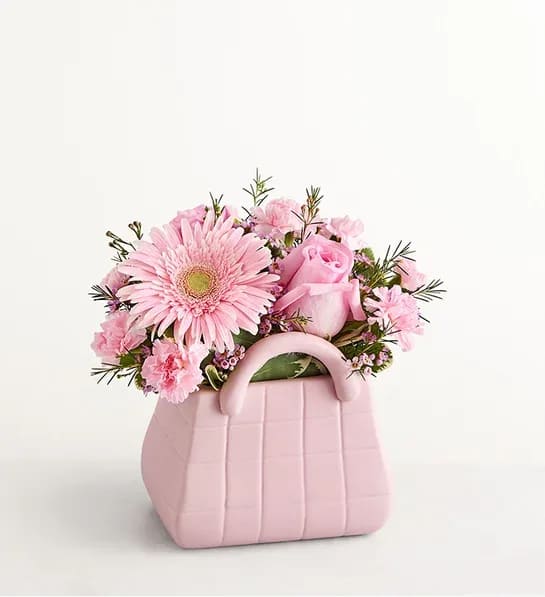 Designer Dreams™ Bouquet - The ultimate arrangement for your favorite fashionista. Roses, Gerbera daisies, and other blooms in delicate shades of pink pop out from the top of our keepsake handbag-shape vase, making this a truly chic gift.