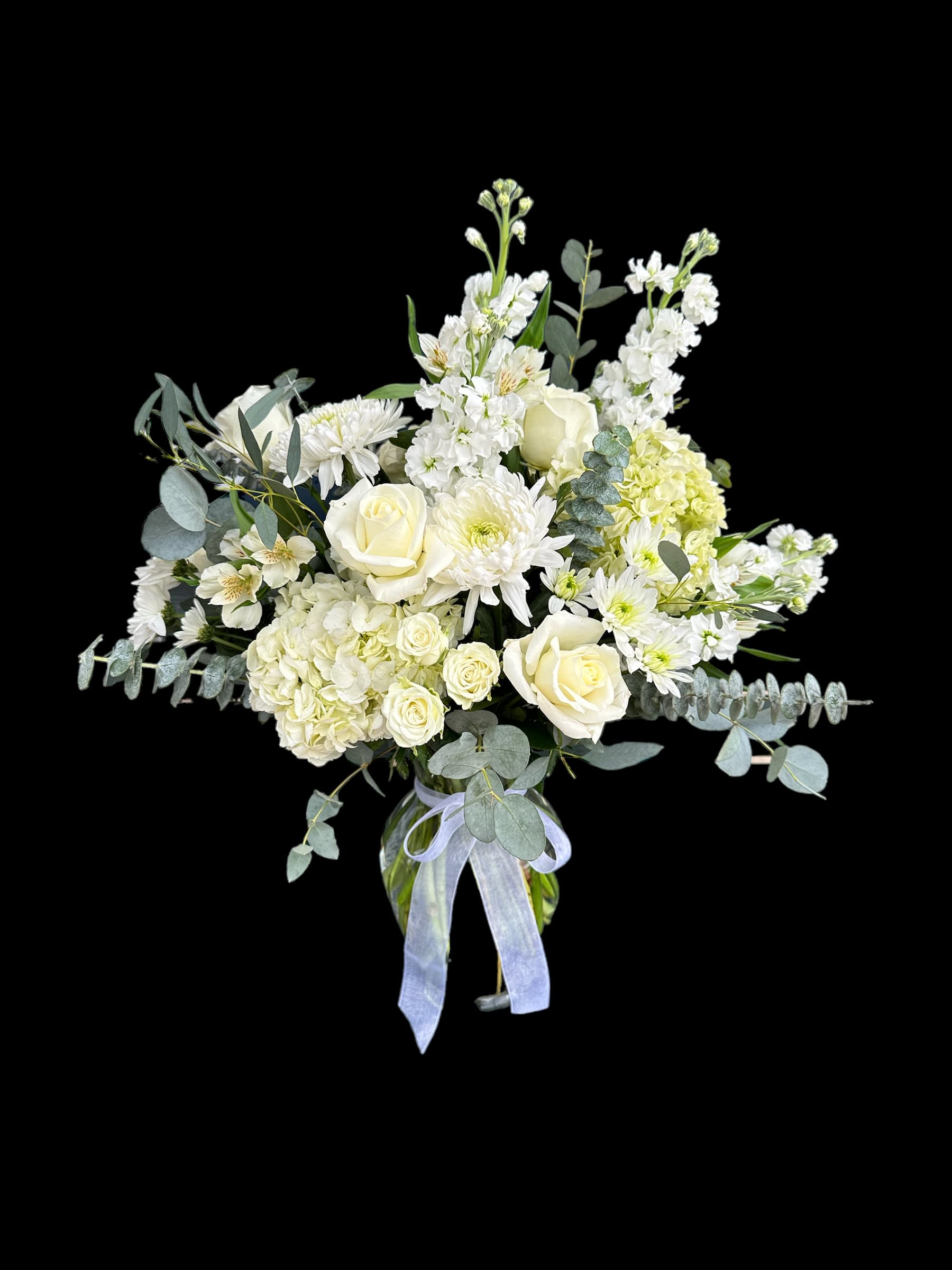White roses and mixed white flowers in a glass vase with a ribbon