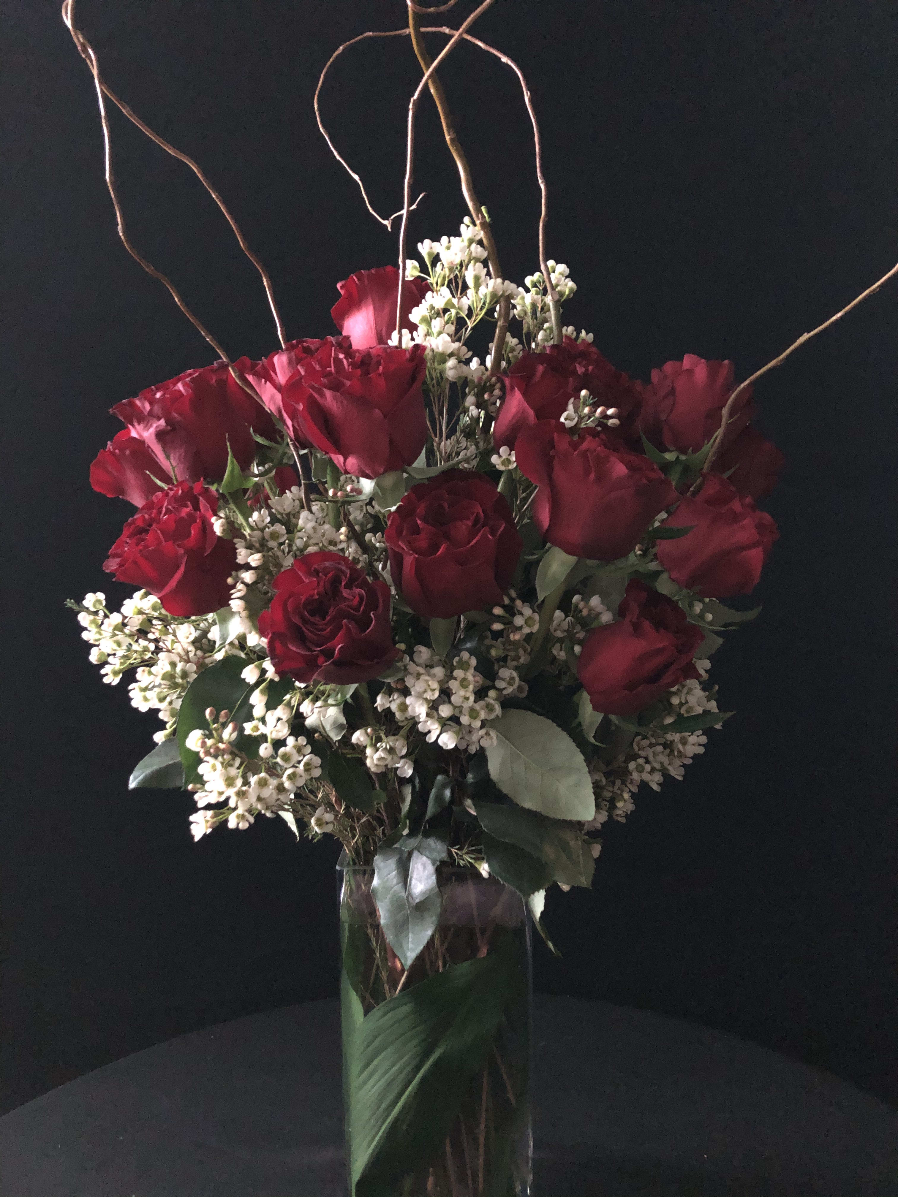 Red roses and white filler flowers in a tall glass vase with curly branches