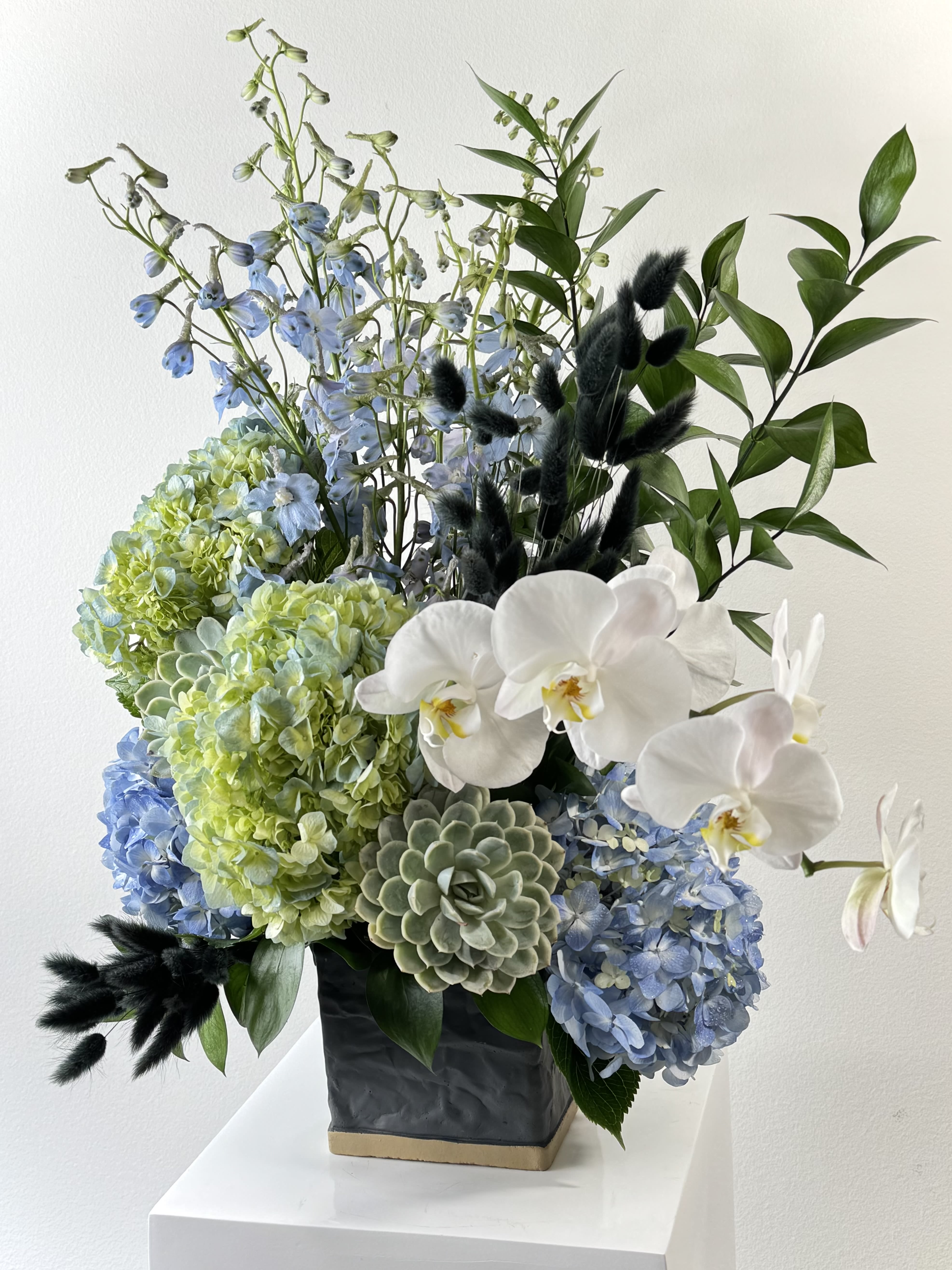 Blue and green floral arrangement with white orchids in a black vase