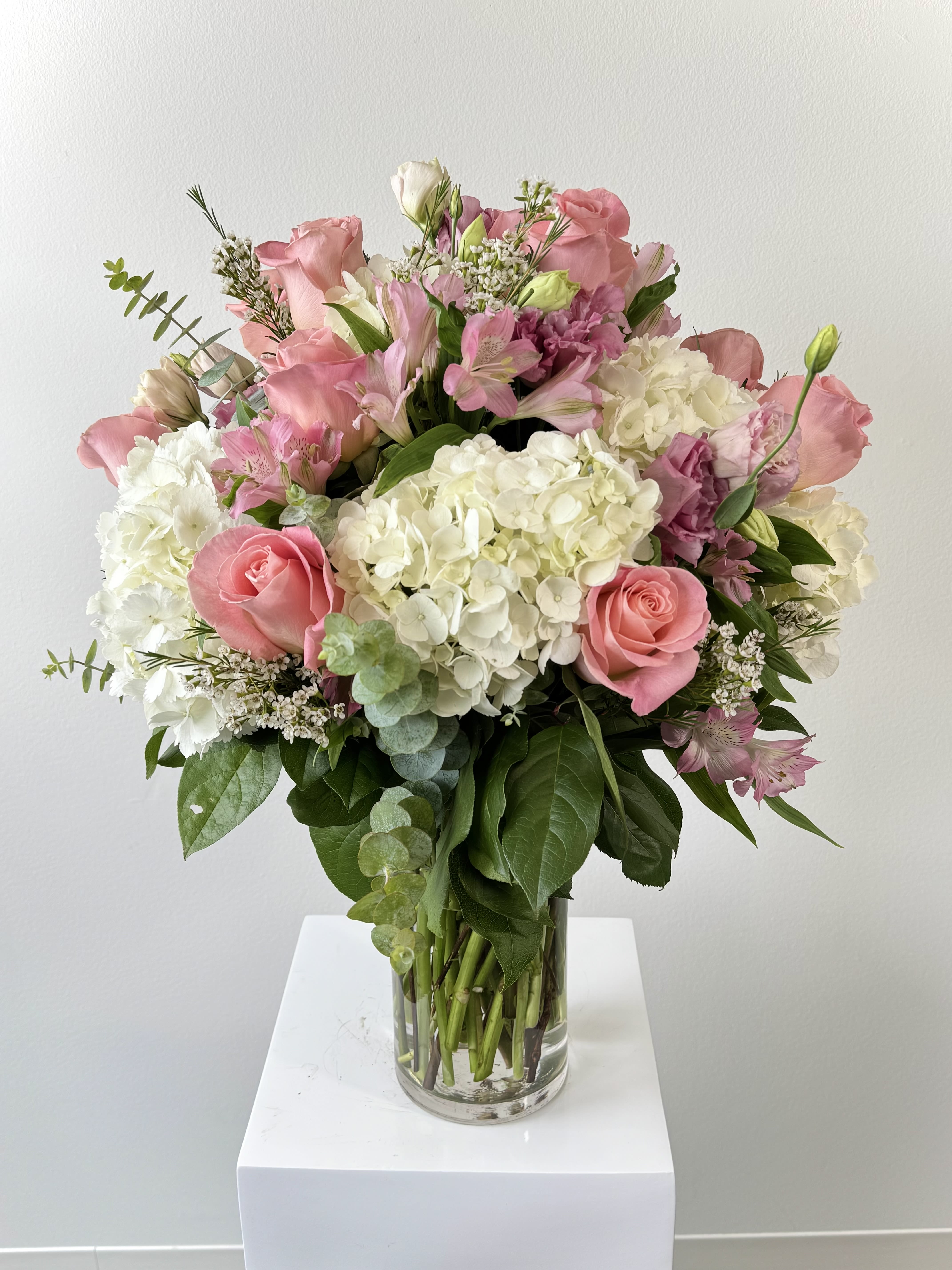 Make Me Blush - Make Me Blush is a sophisticated bouquet blends timeless elegance with modern "quiet luxury" textures, making it the perfect choice for high-end gifting and home decor. At its heart, this arrangement features a dozen blush pink roses, symbolizing deep admiration, grace, and refined femininity. These iconic blooms are nestled in a lush base of premium white hydrangea, which adds voluminous texture and represents heartfelt gratitude and purity. To create a layered, multi-dimensional look, our designers incorporate pink alstroemeria (Peruvian lilies), signifying enduring friendship and devotion, alongside the delicate, ruffled petals of pink lisianthus. Why Choose "Make Me Blush" for 2026? - On-Trend Palette: Perfectly aligns with the 2026 "Whisper" and "Rejuvenate" trends, emphasizing soft textures and fluid tranquility. - Versatile Gifting: Ideal for anniversaries, birthdays, or romantic "just because" moments. - Long-Lasting Beauty: Both lisianthus and alstroemeria are prized for their exceptional vase life, ensuring your sentiment lingers. Elevate your next occasion with this sculptural, garden-inspired design that speaks volumes without saying a word. Whether as a centerpiece or a surprise delivery, "Make Me Blush" is the definition of modern elegance. Order now for same-day delivery!