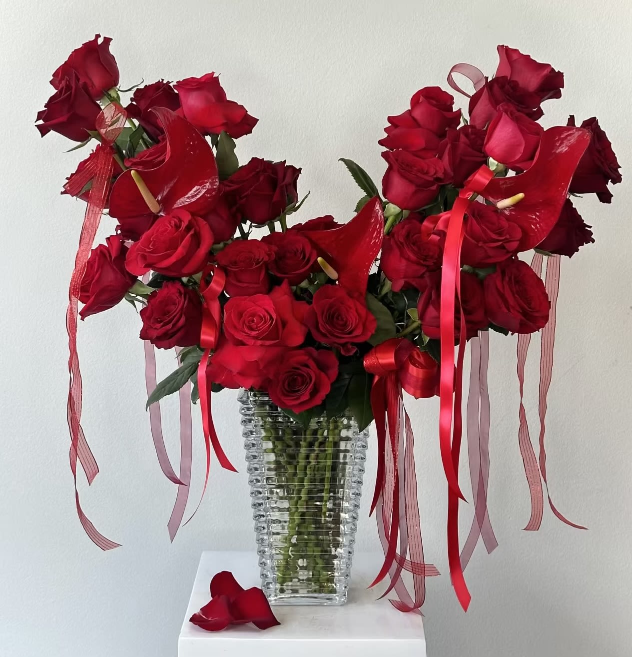 Red roses arranged in a clear ribbed vase with red ribbons