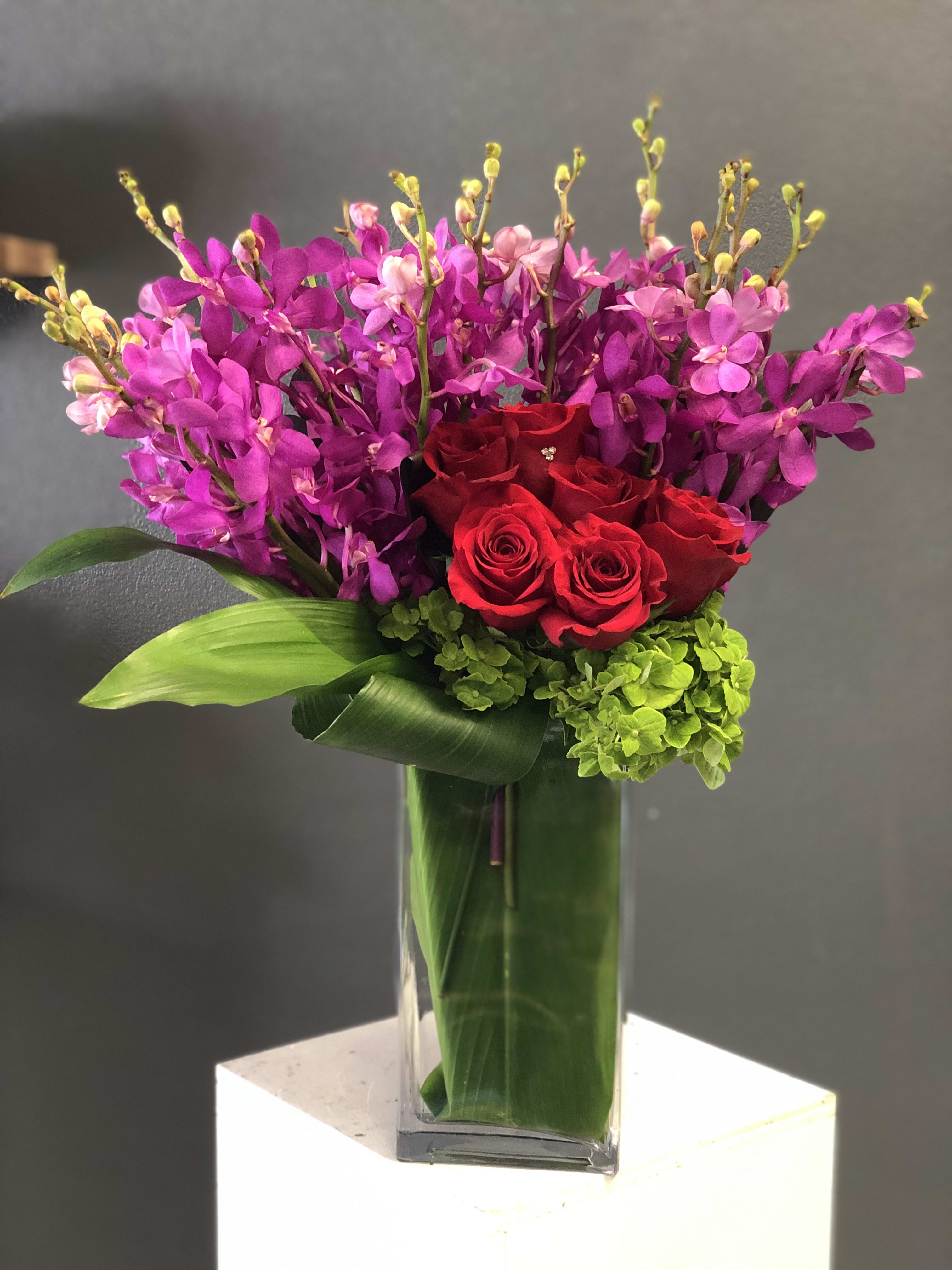 Red roses and purple orchids in a clear glass vase