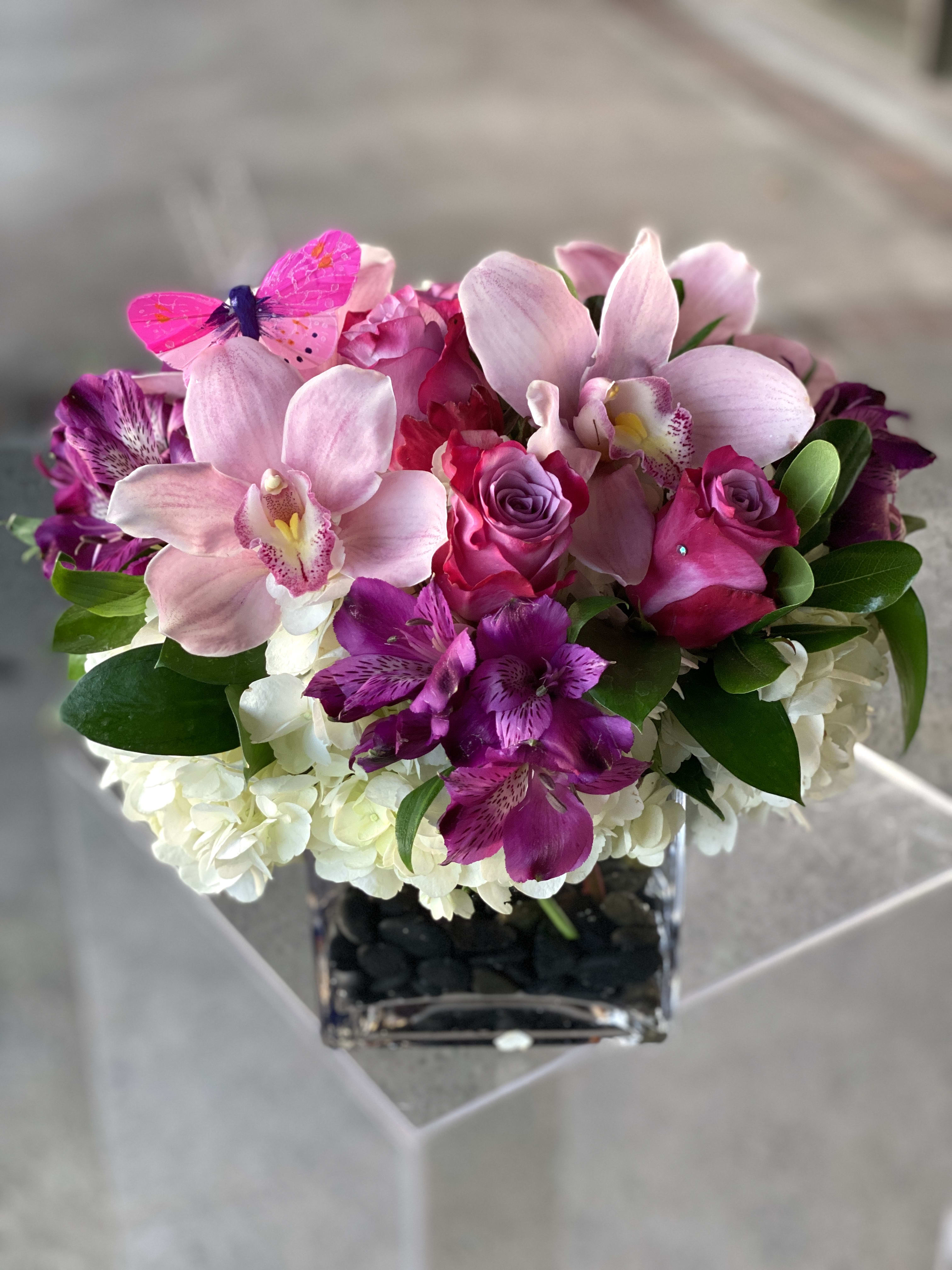 Pink orchids and roses arranged in a square glass vase