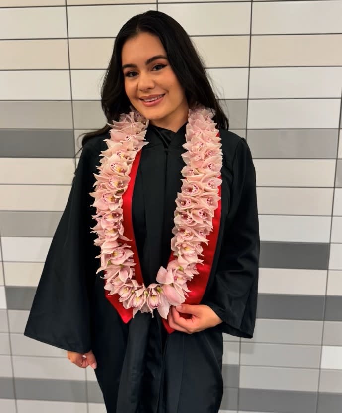 Woman in a graduation gown wearing a pink flower lei
