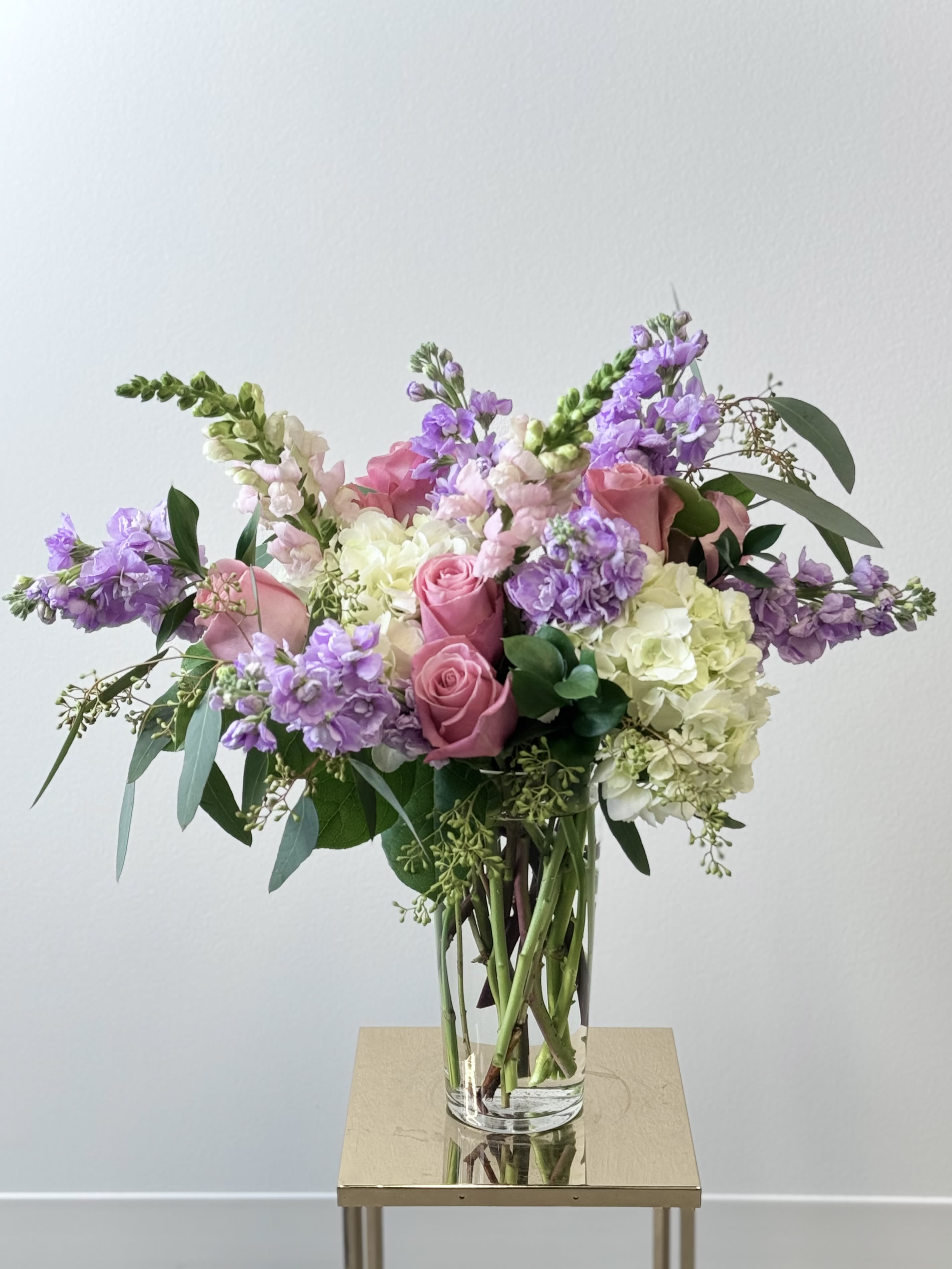 Pink roses and purple blooms in a clear glass vase