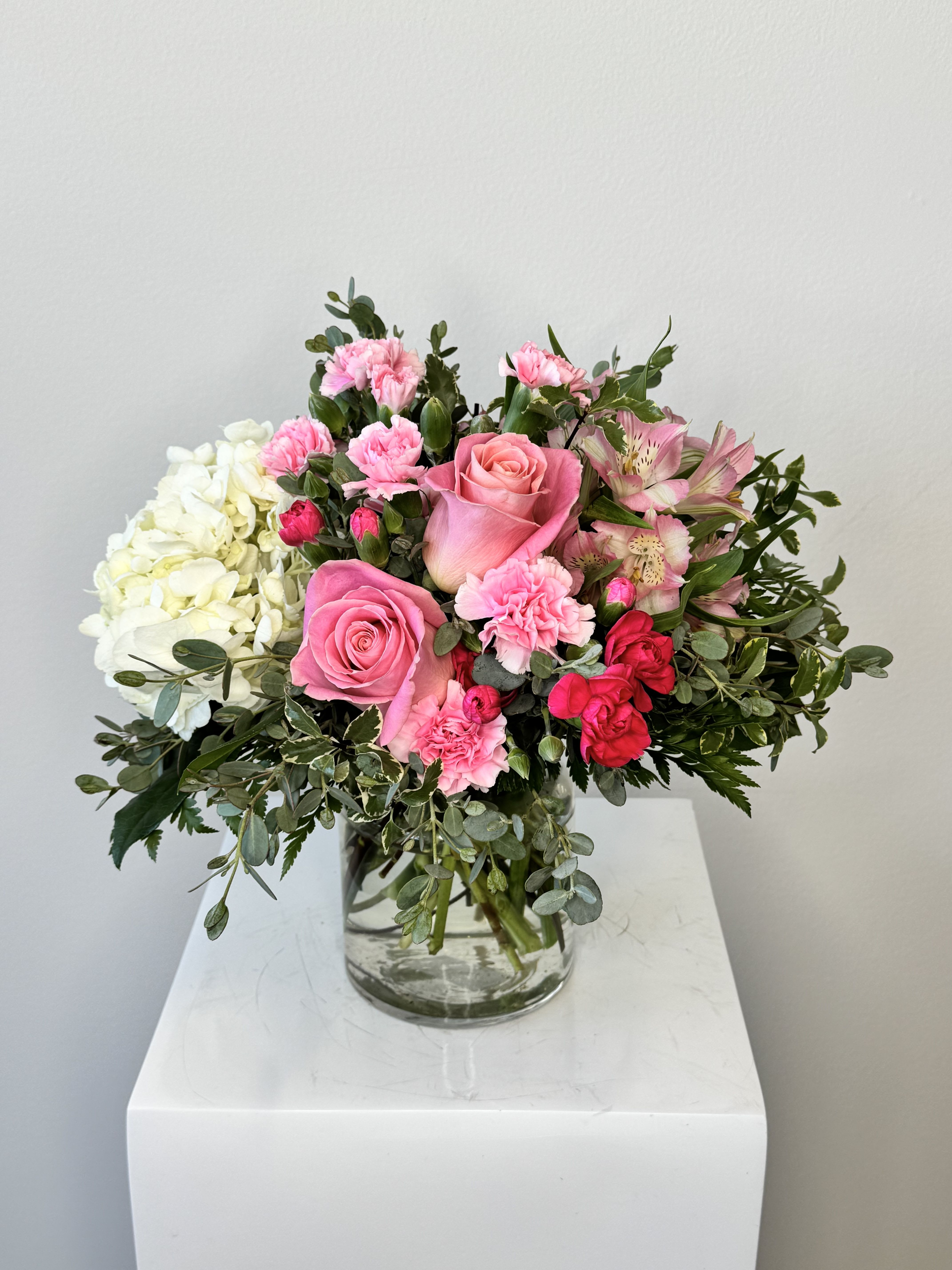 Pink roses, carnations, and white hydrangeas arranged in a clear glass vase