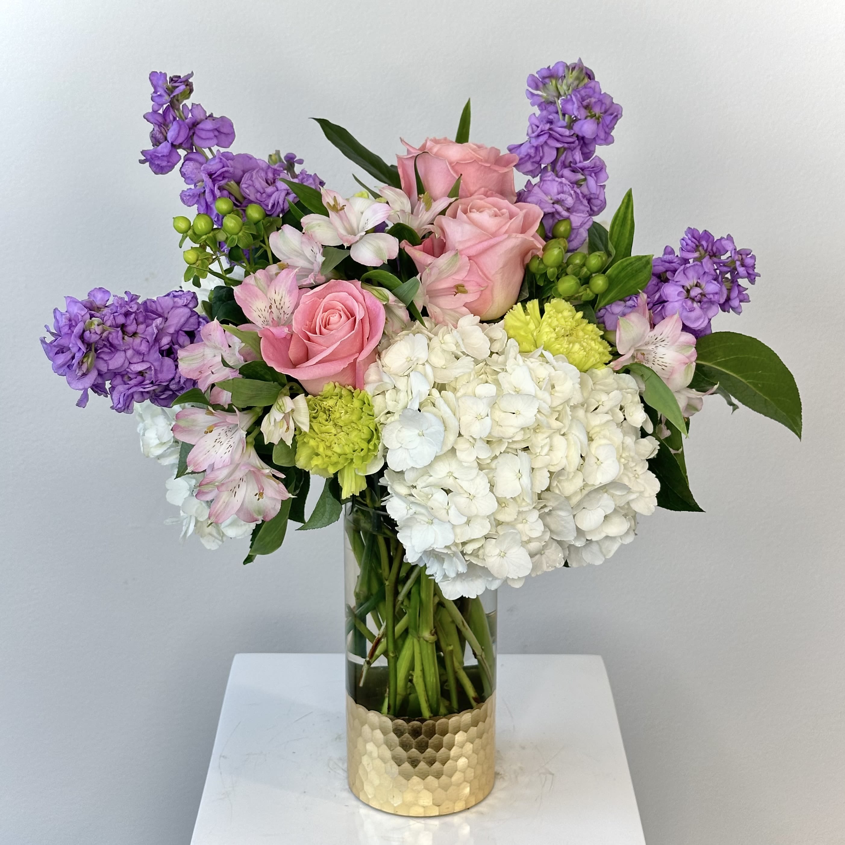 Pink roses, white hydrangea, and purple flowers in a gold vase