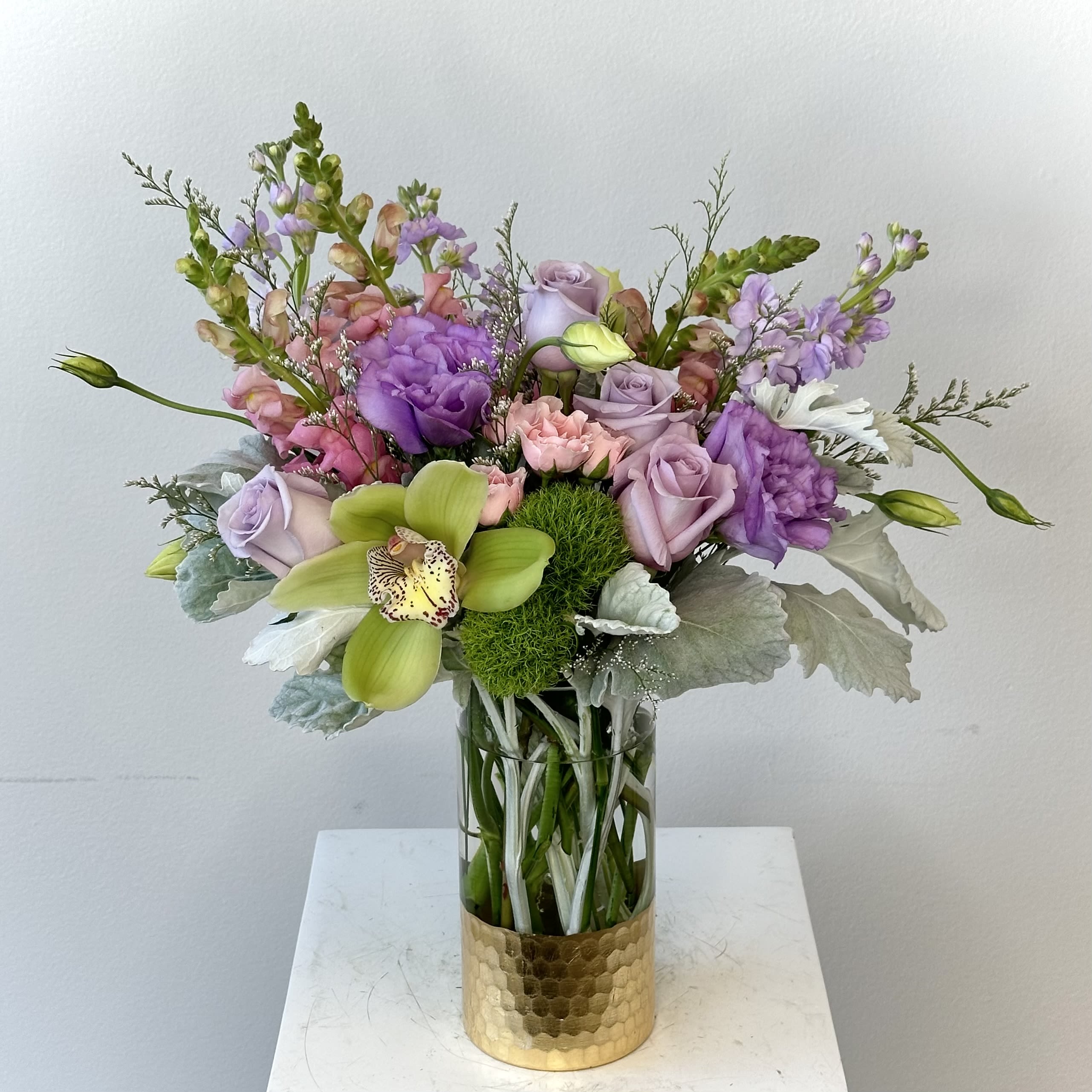 Snuggle Bouquet - PET-SAFE REMINDER: While the Snuggle Bouquet is designed using flowers that are generally considered pet-friendly, no flower or plant should be intentionally eaten by pets. As a precaution, we recommend displaying this arrangement in a location that is out of reach of curious cats and dogs, as ingesting any flowers or foliage may cause stomach upset or other discomfort.  The Snuggle Bouquet is a medium-sized floral arrangement designed to bring comfort, beauty, and vibrant color to any occasion. This charming bouquet features a striking green cymbidium orchid, elegant purple lisianthus, soft lavender roses, graceful pink snapdragons, fragrant lavender stock, delicate pink spray roses, playful green dianthus balls, and soft dusty miller. The harmonious blend of lavender, pink, and fresh green blooms creates a lush, garden-inspired design that feels both modern and timeless.  Perfect for birthdays, thank-you gifts, get-well wishes, celebrations, or simply brightening someone's day, the Snuggle Bouquet is handcrafted with premium fresh flowers and expert floral artistry. If you're looking for a pet-friendly flower arrangement with a soft, elegant color palette, the Snuggle Bouquet is a beautiful choice that delivers warmth, charm, and lasting beauty in every bloom.