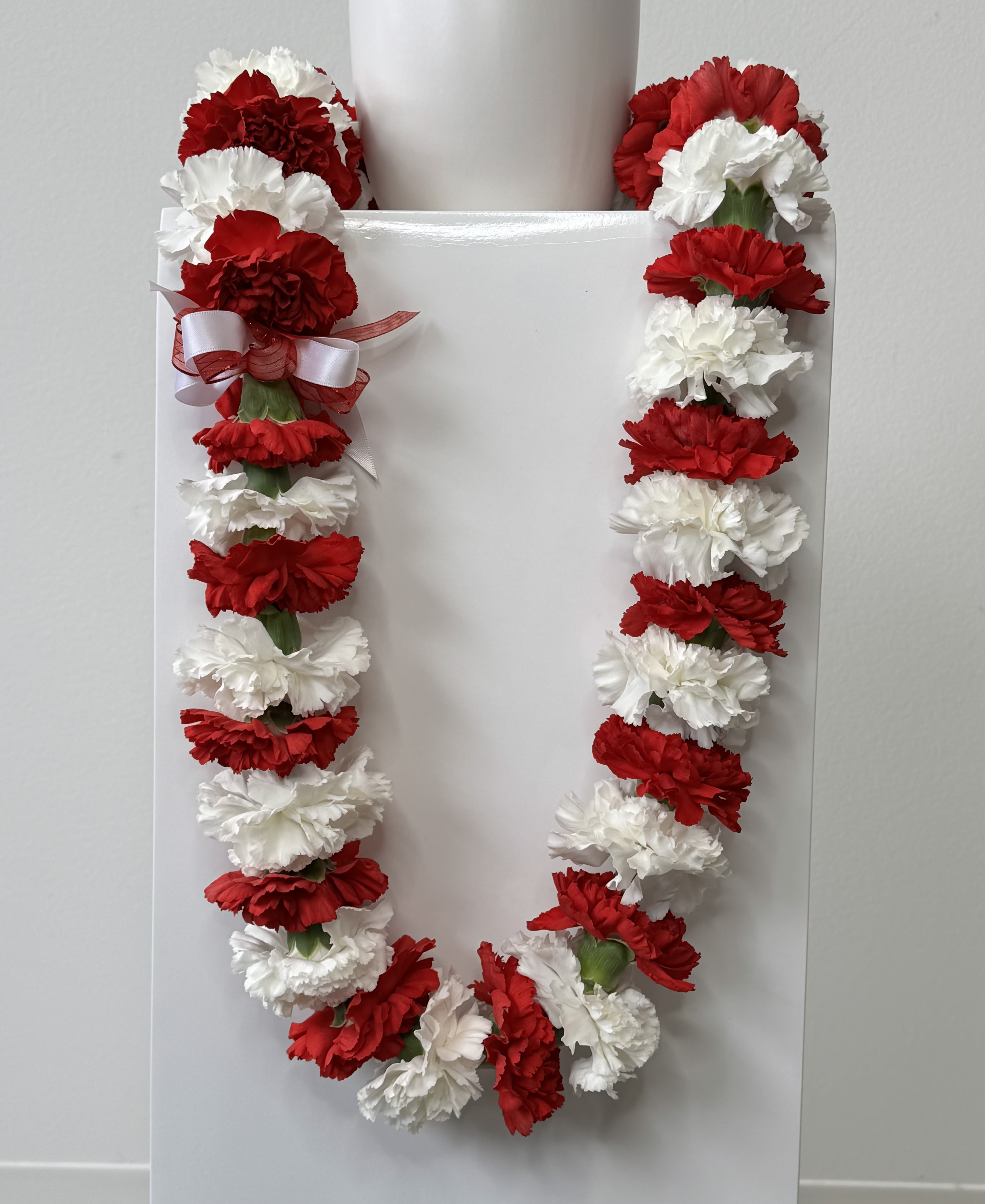 Carnation Lei - Celebrate your graduate with a classic carnation graduation lei, a timeless symbol of honor, achievement, and celebration. Available in both single strand and double strand options, these leis are handcrafted in-house with fresh carnations for a full, vibrant look that stands out on graduation day.  Offered in white, light pink, light green, red, or a variety of these colors, each color carries its own meaning while creating a beautiful, eye-catching presentation for ceremonies and photos. Carnation leis are known for their durability and long-lasting freshness, making them a perfect choice for all-day wear and keepsake memories.  Each lei is carefully designed to ensure a balanced, elegant drape, whether you choose a single strand for a classic look or a double strand for a fuller, more statement-making style. Ideal for high school and college graduations, these leis add a meaningful and celebratory touch to any milestone achievement.  Looking for a custom color? Additional colors are available upon request as a special order. Please note that all custom color requests require a minimum two-week notice to ensure availability and quality.  Order your carnation graduation lei today for pickup or delivery, and celebrate your graduate with a beautiful, traditional floral piece made just for their big day.  Please allow at least a 1 day heads-up for us to create your lei.