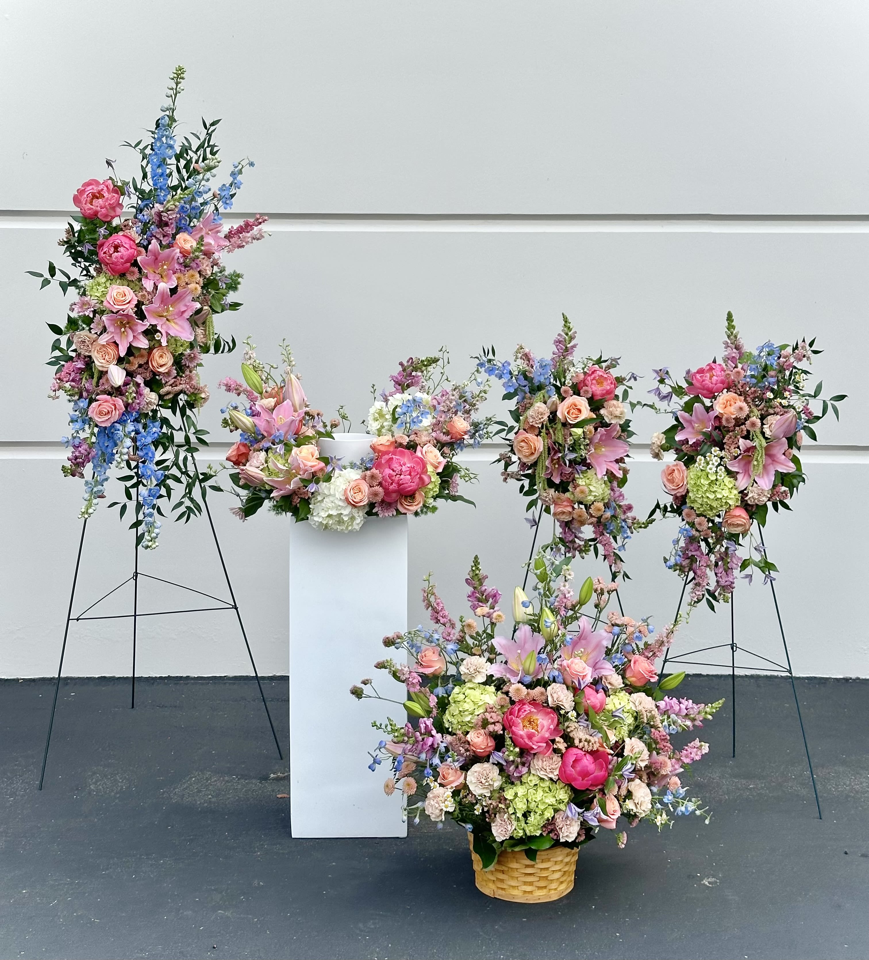 Large floral arrangements with pink, blue, and peach blooms in baskets and on stands