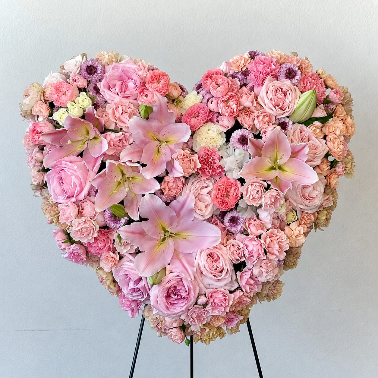 Heart-shaped pink floral arrangement with roses, carnations, and lilies on a stand
