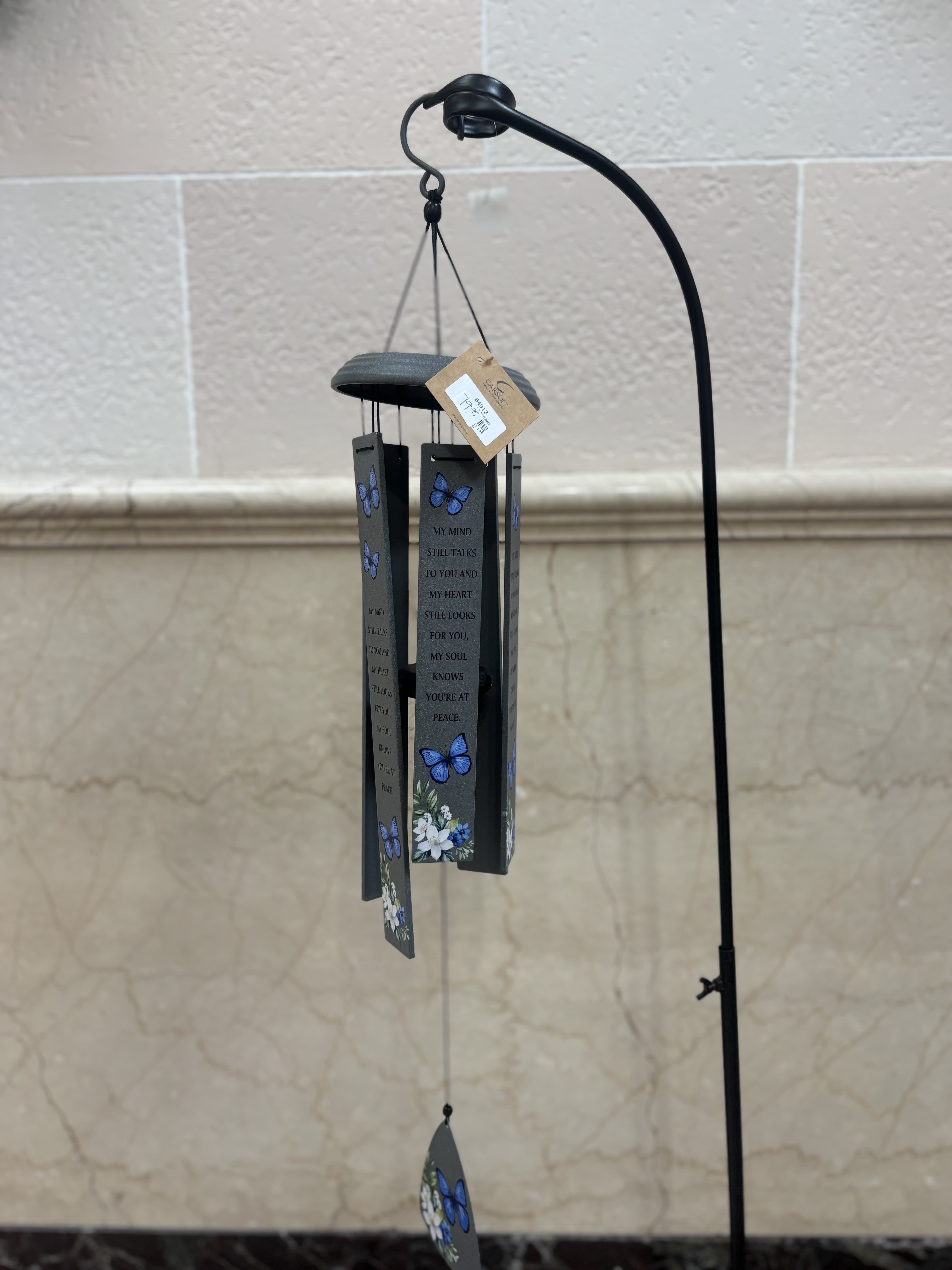 Gray memorial wind chime with blue butterflies and white floral accents hanging from a tall black metal stand.