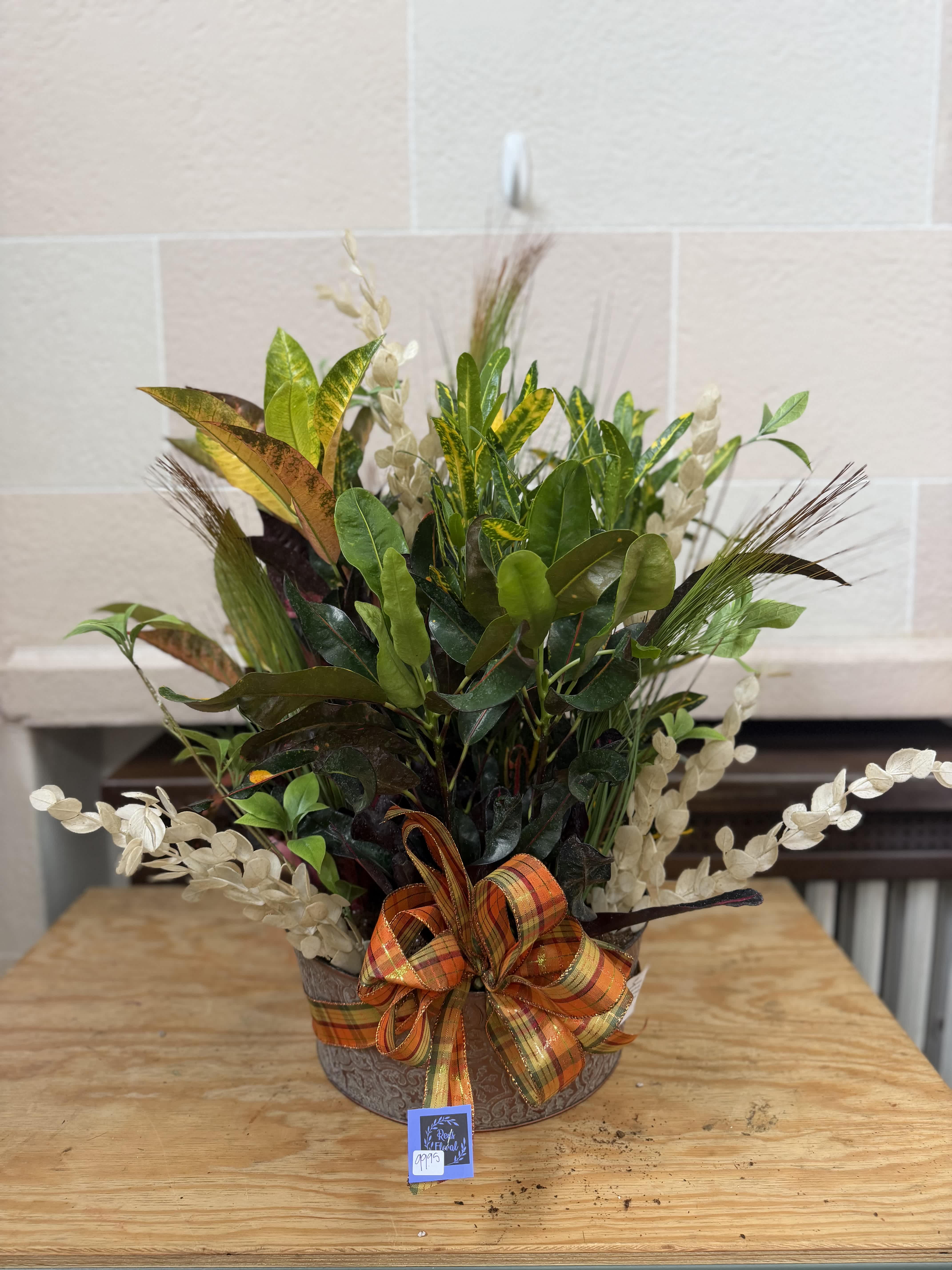 Mixed foliage arrangement in a decorative container with an orange plaid bow