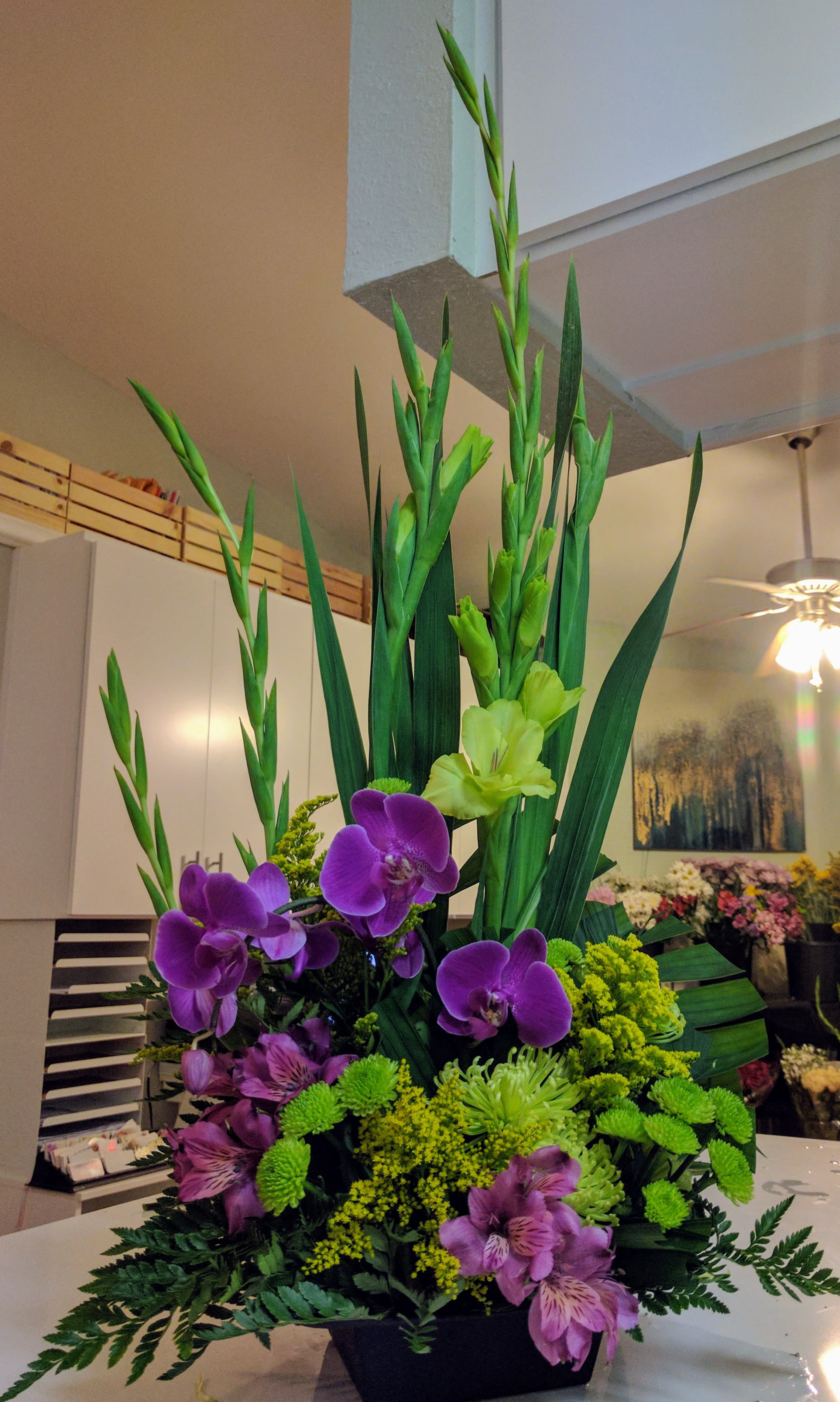 Tall floral arrangement with purple orchids and green blooms in a black container