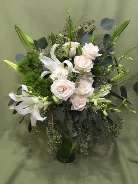 White roses and lilies in a glass vase with dark foliage