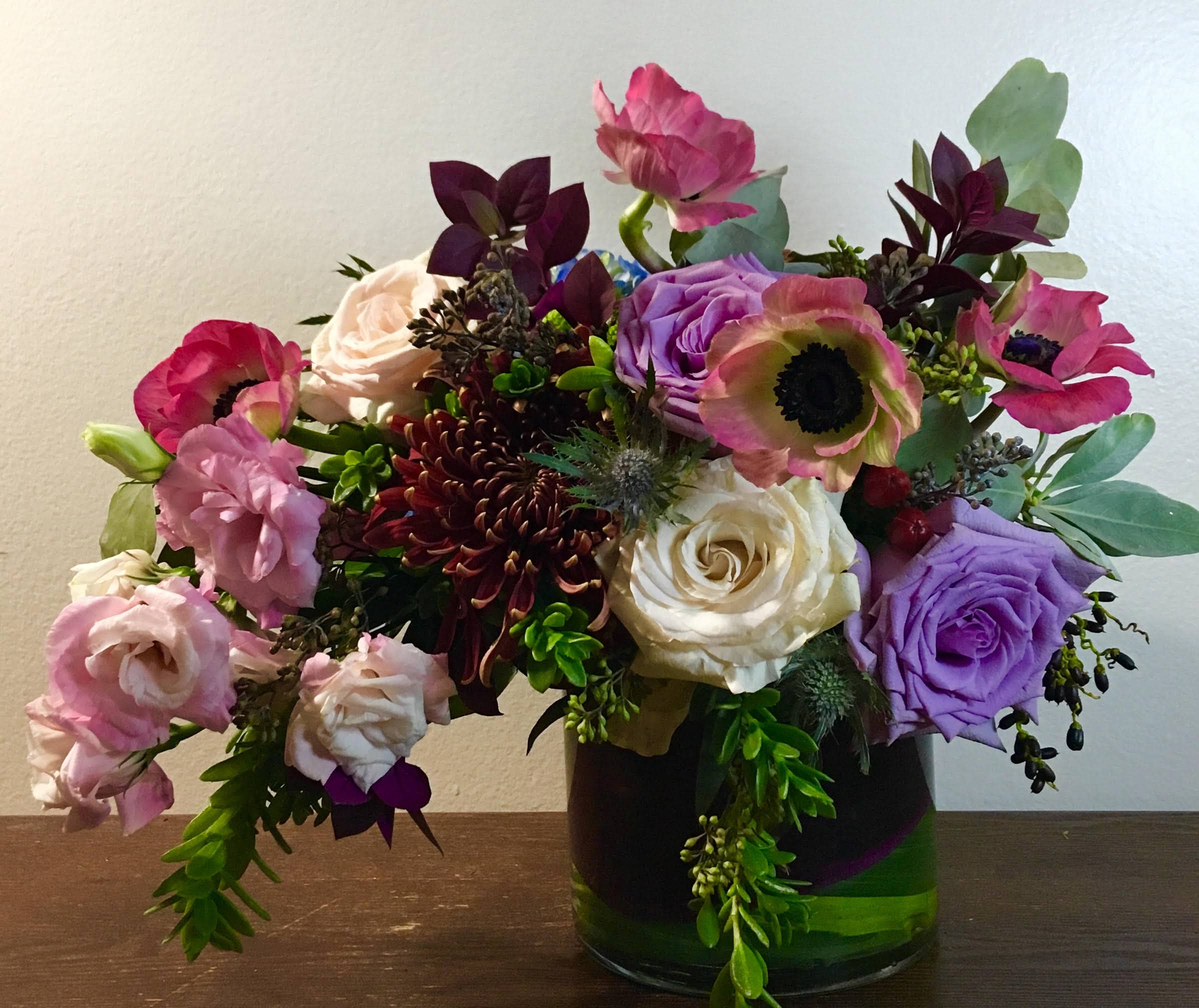 Mixed bouquet of roses, poppies, and chrysanthemums in a glass vase