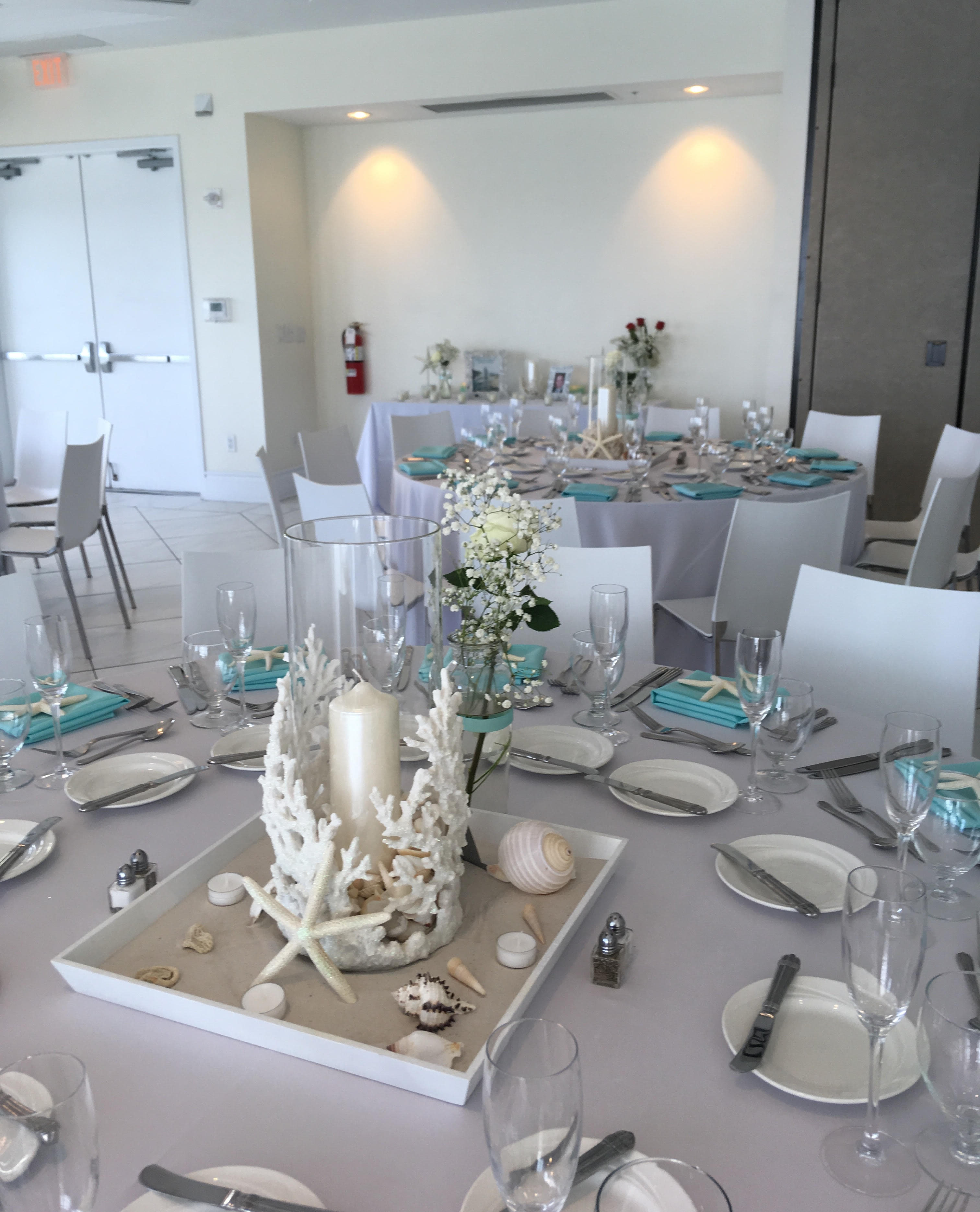 White floral centerpieces on round banquet tables with seashell decor