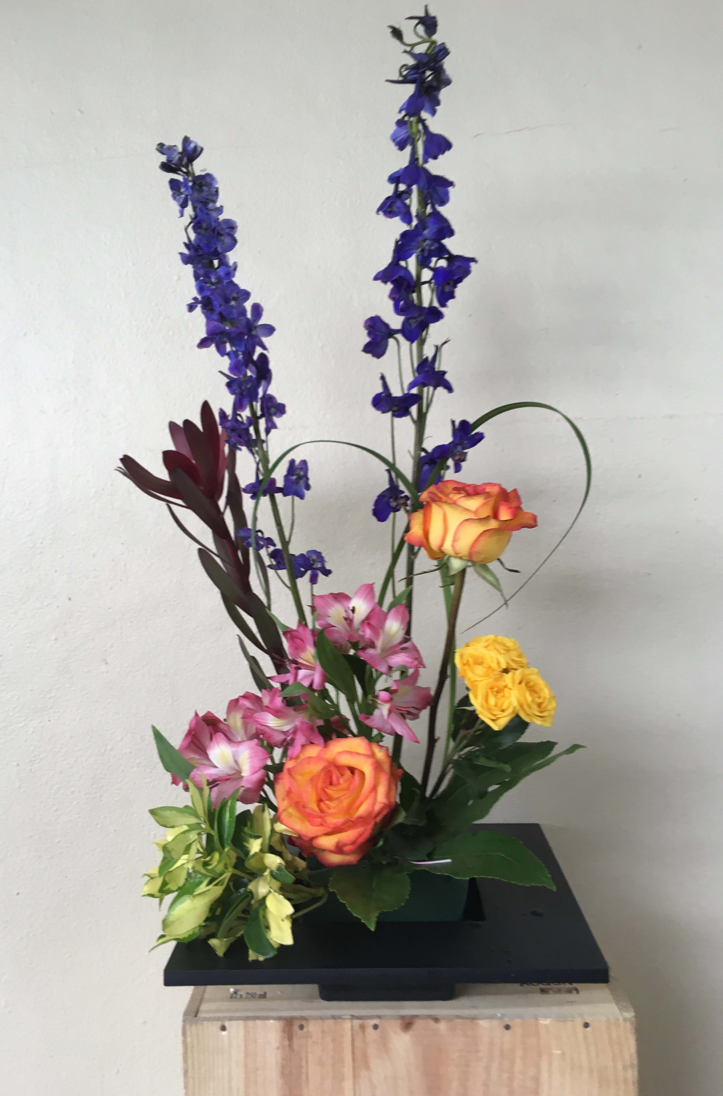 Tall floral arrangement with orange roses, pink alstroemeria, and blue delphinium