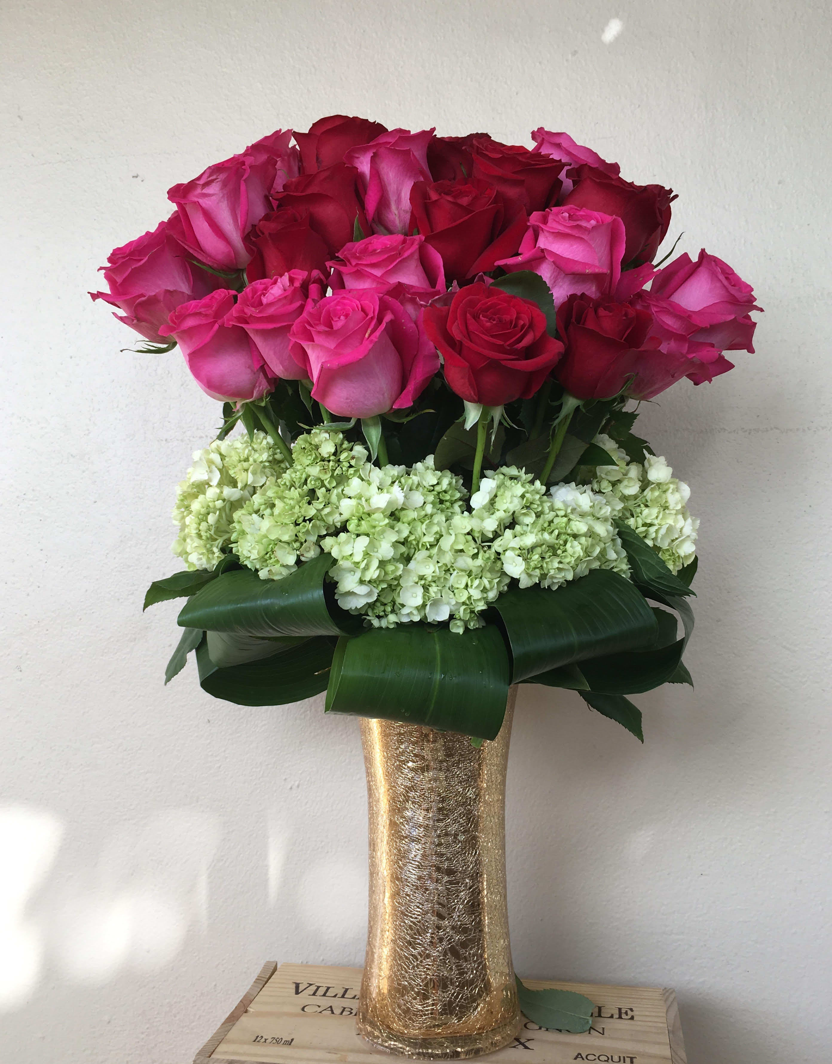 Bouquet of pink and red roses in a gold vase with white hydrangeas