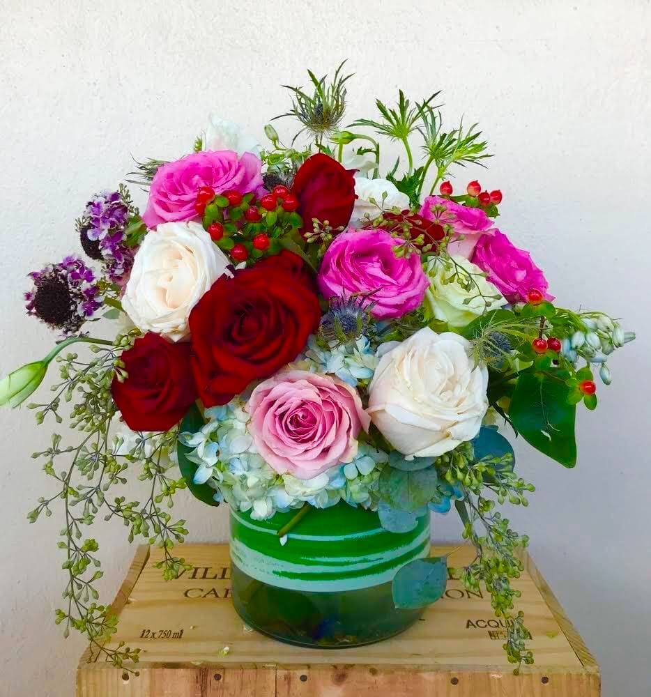 Bouquet of red, pink, and white roses in a green glass vase